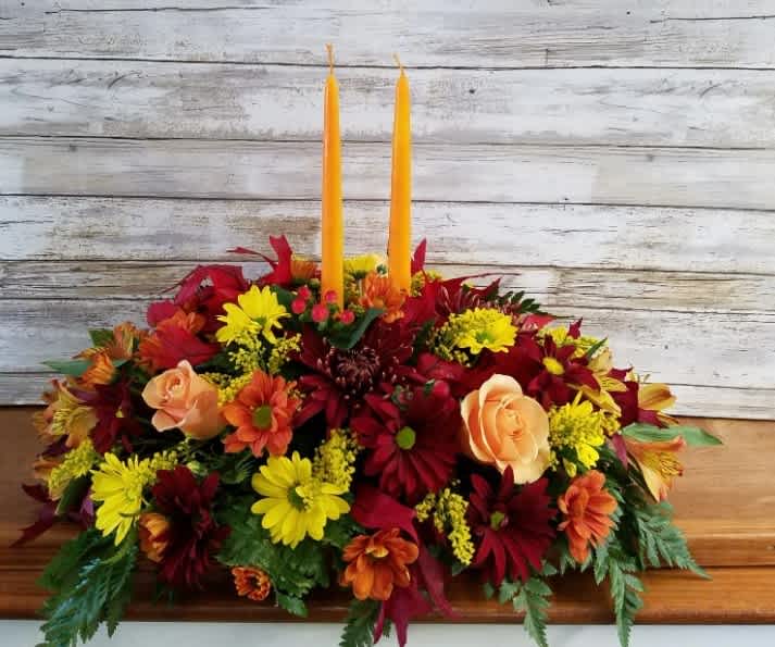 Warm Wishes Centerpiece by Art &amp; Flowers -  A true classic, the Warm Wishes centerpiece brings timeless elegance to your Thanksgiving table. Featuring vibrant fall blooms in rich autumn tones and two glowing candles, it creates a warm and inviting ambiance perfect for your holiday celebrations.  Flowers may vary from photo, but style will be as pictured in a fall palette. 