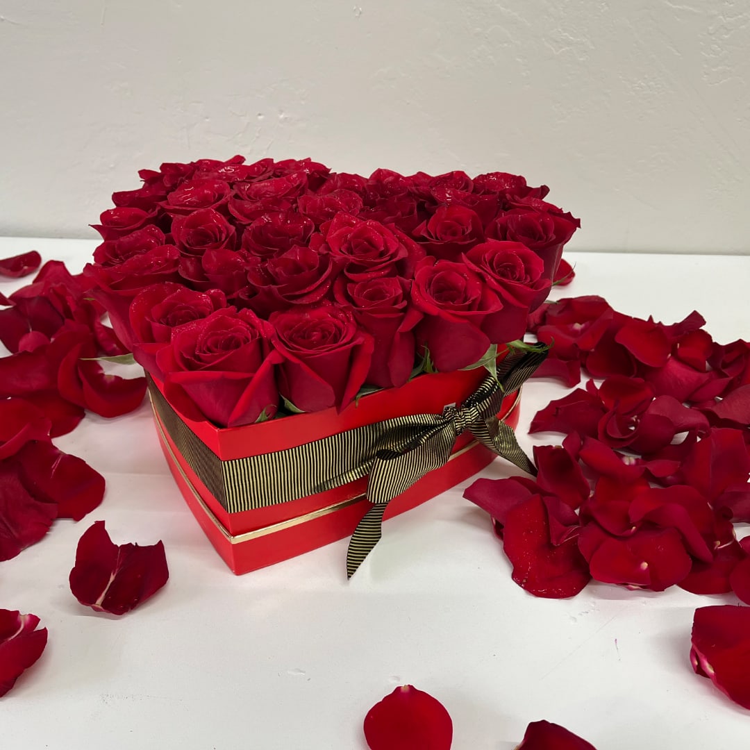 Red roses arranged in a heart-shaped gift box with scattered petals