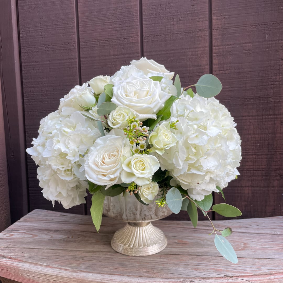 White roses and hydrangeas arranged in a silver pedestal vase