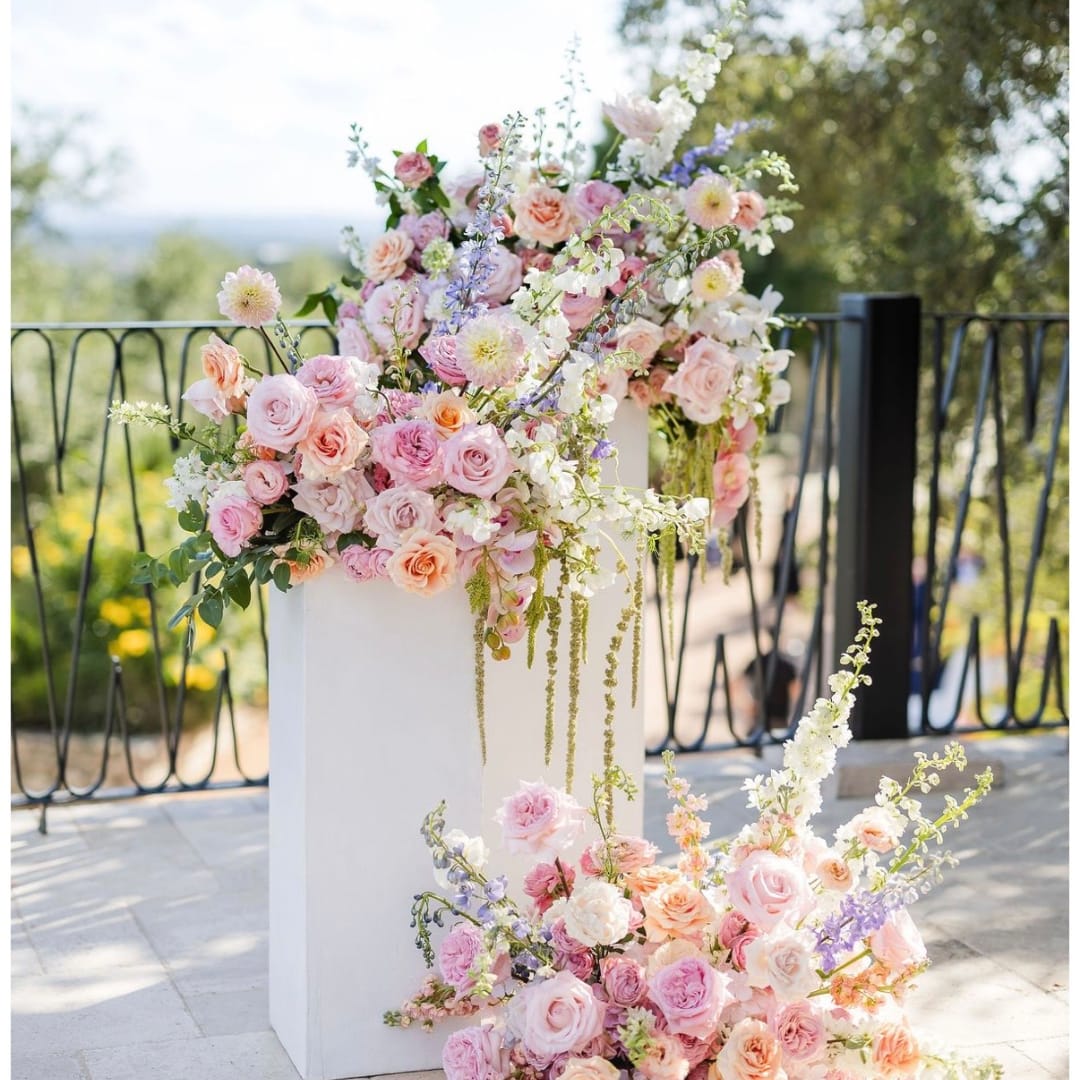 Pastel floral wedding arrangement with roses and mixed blooms on white pedestals