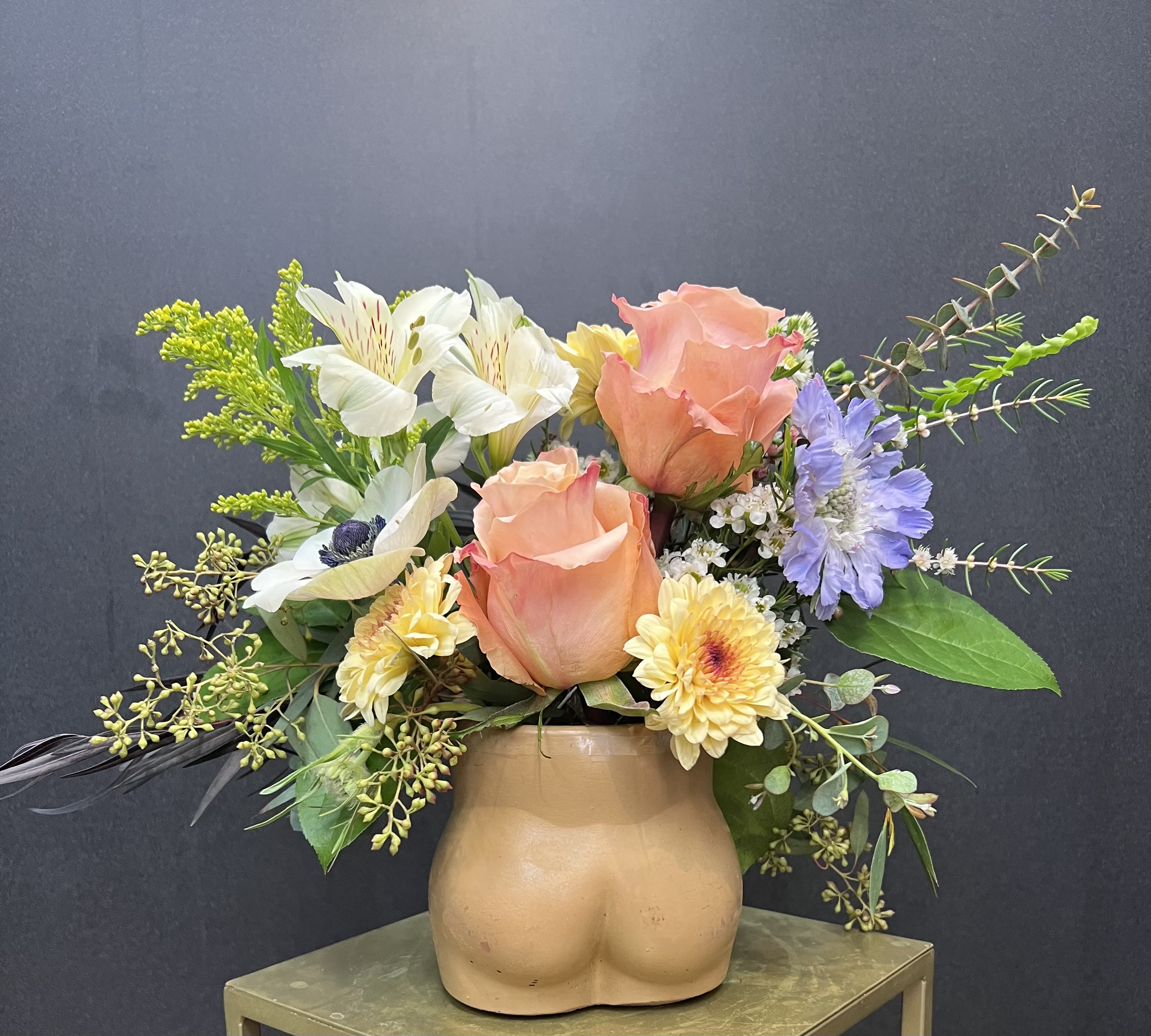 Peach roses and mixed flowers in a tan ceramic vase shaped like a torso