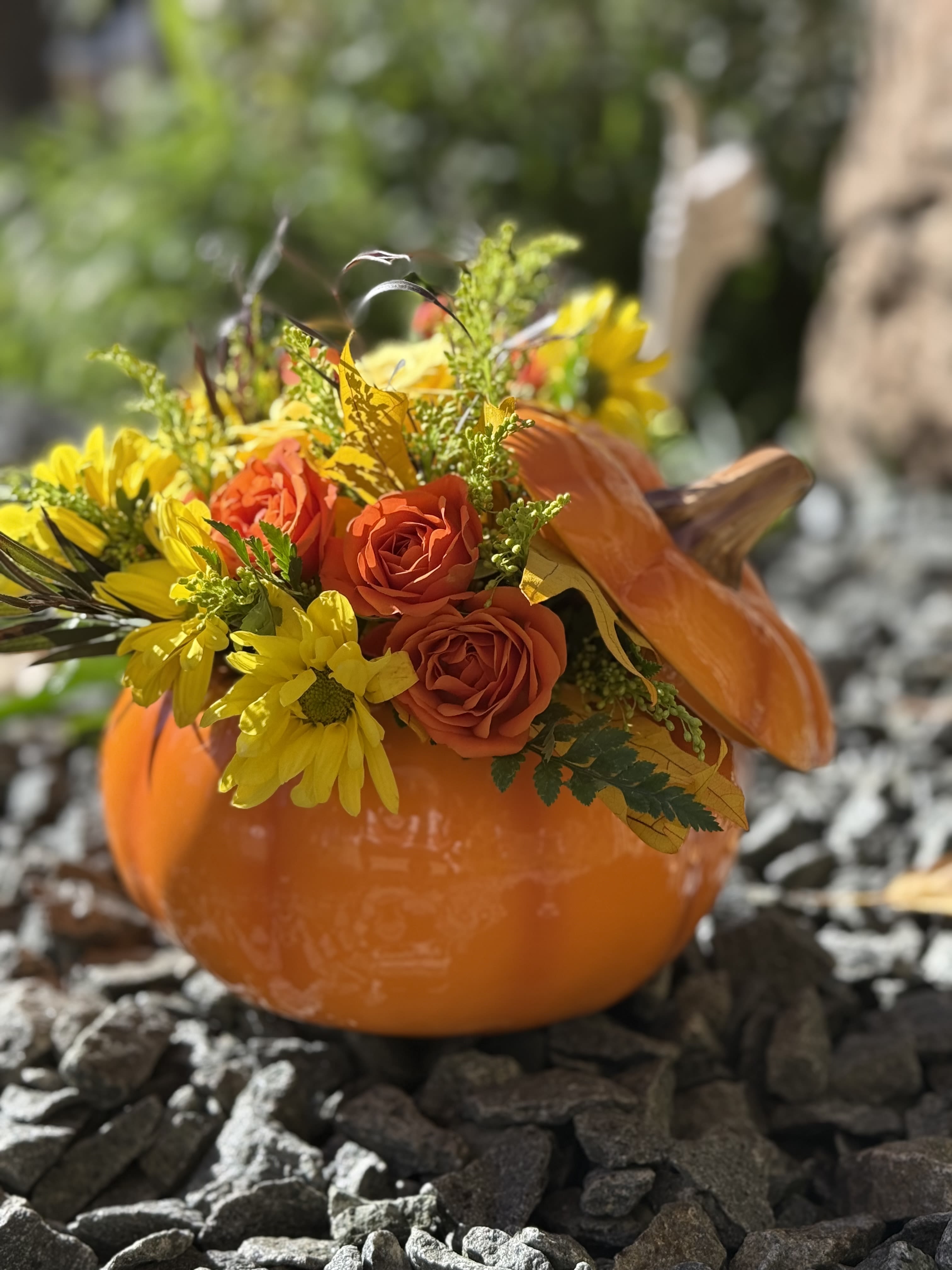 Orange pumpkin container filled with orange roses and yellow daisies