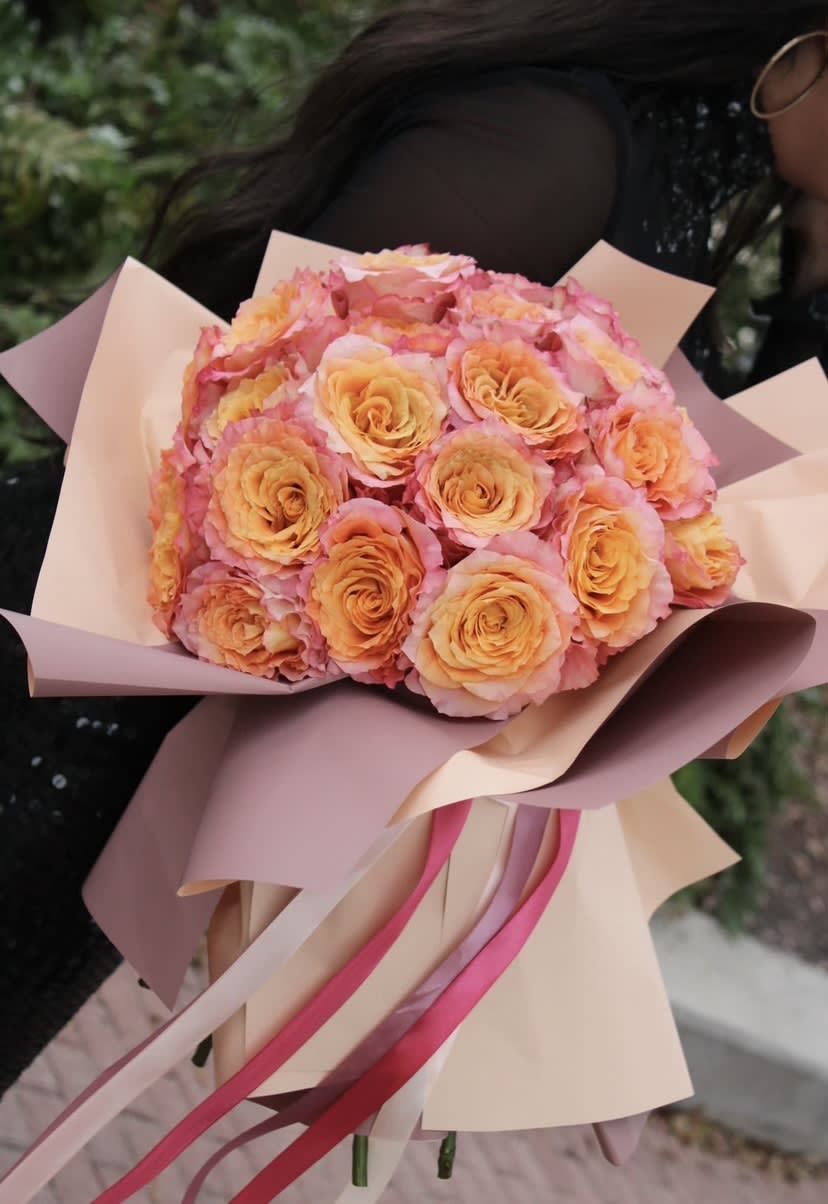 Bouquet of peach and pink roses wrapped in blush paper with ribbons