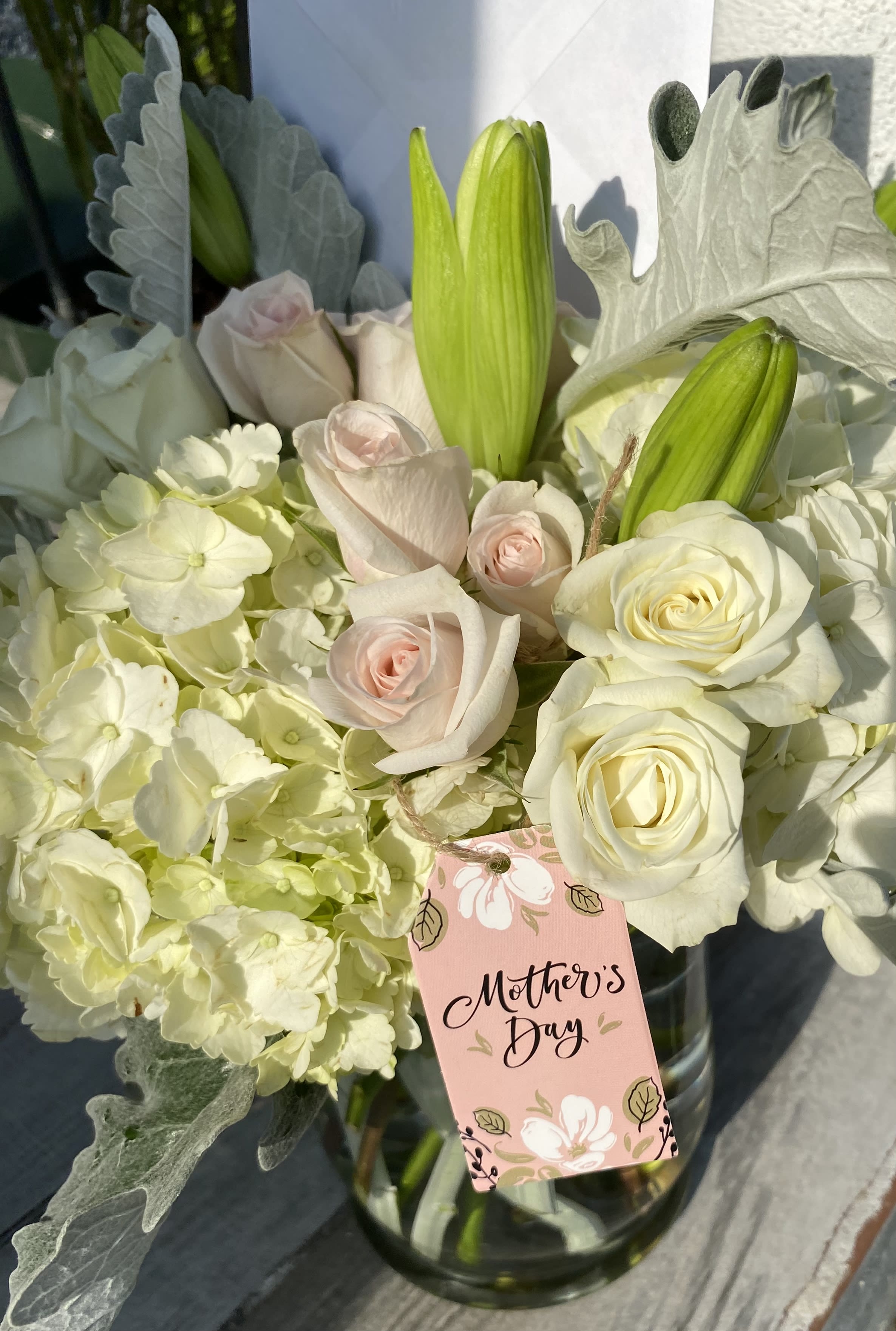 White roses and pale hydrangeas with green lily buds in a glass vase