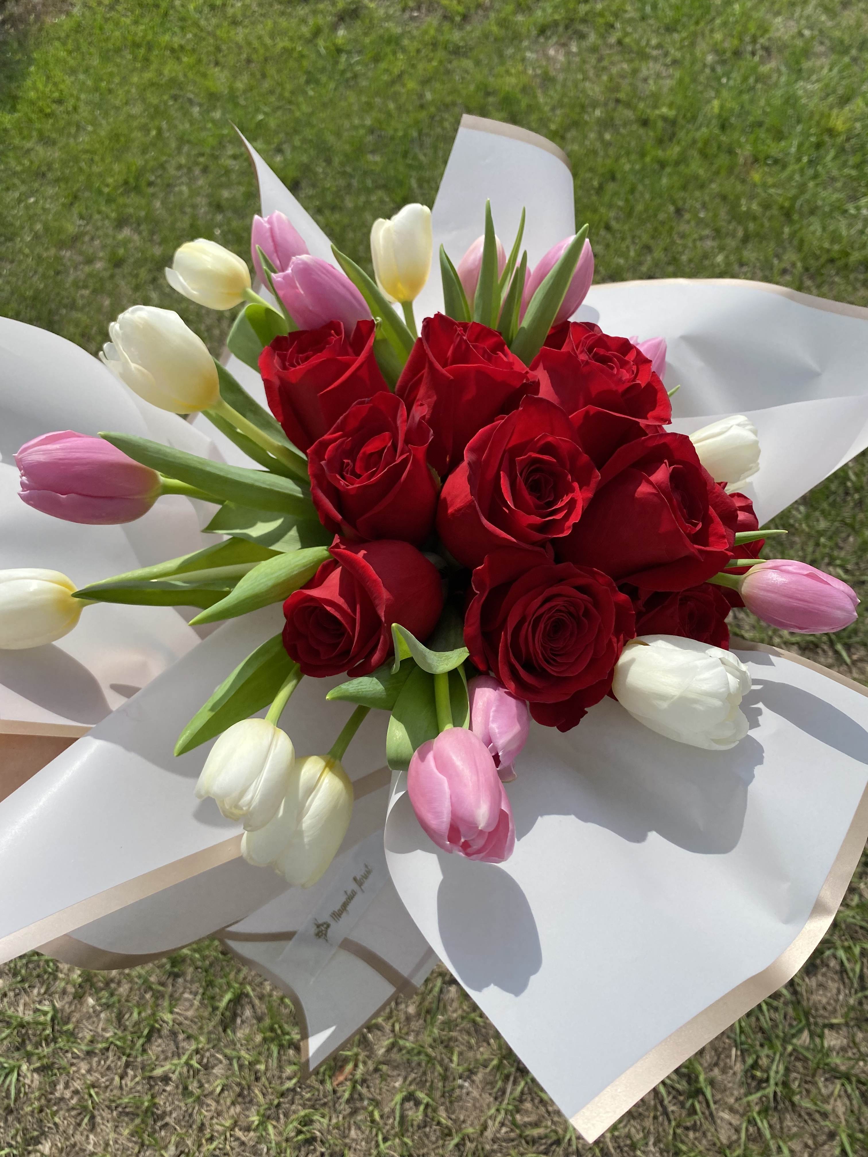 Bouquet of red roses and pink and white tulips wrapped in white paper