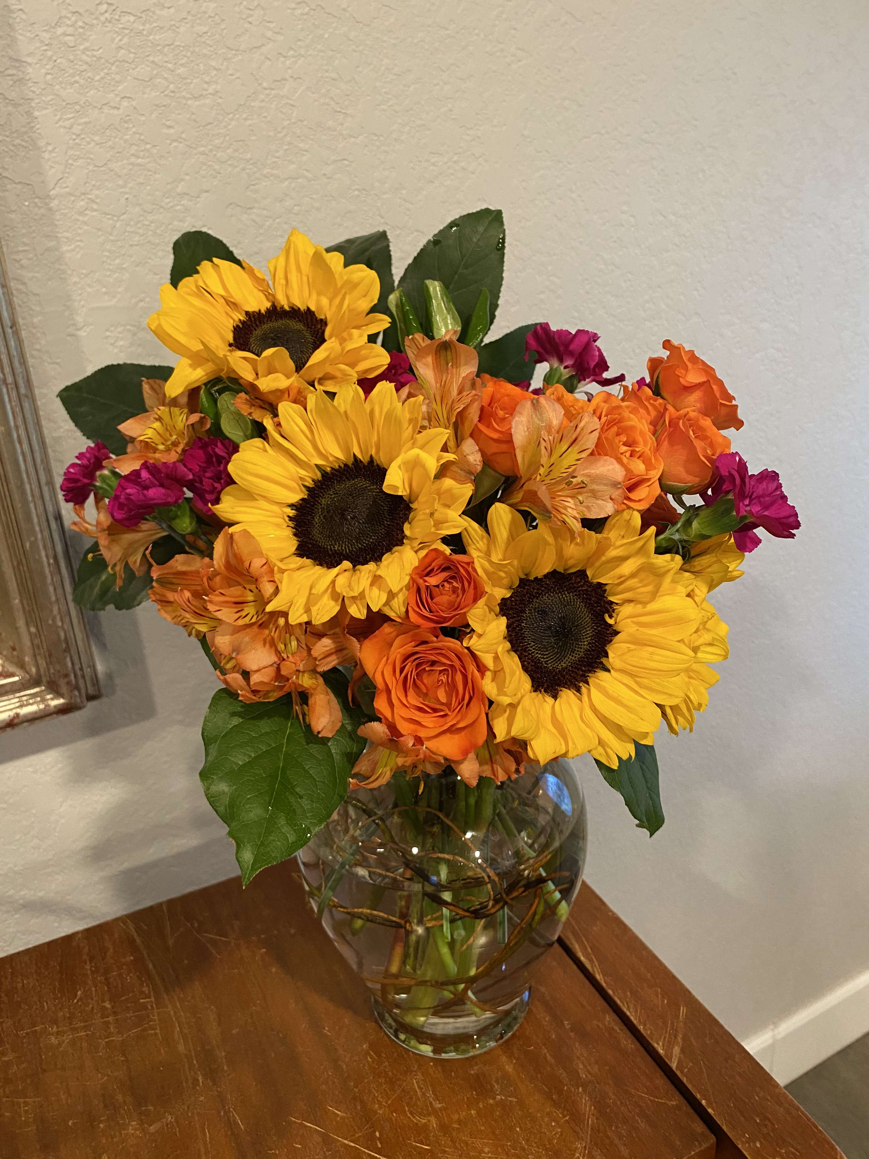 Bouquet of sunflowers, orange roses, and magenta flowers in a glass vase