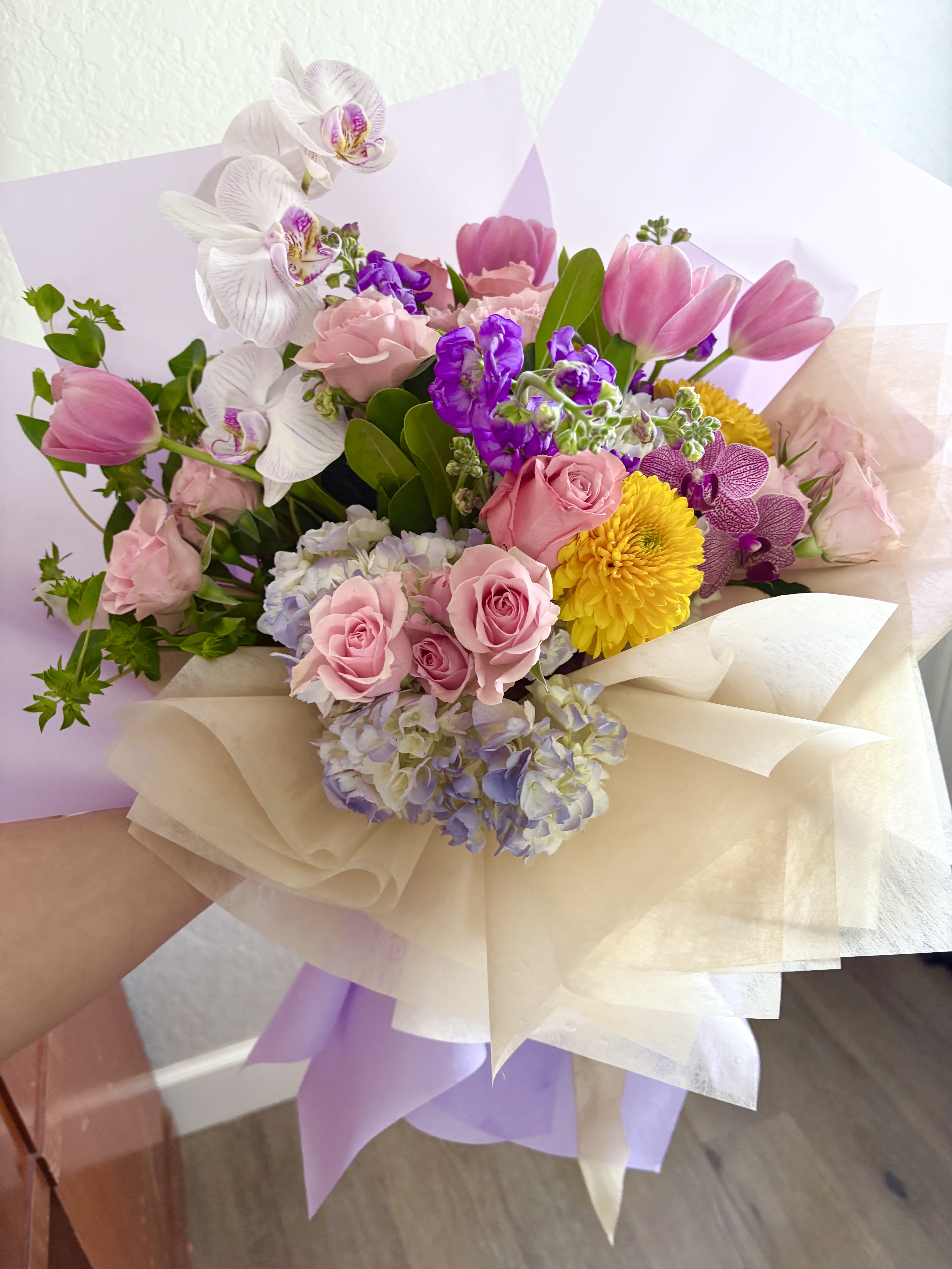Bouquet of pink roses, tulips, orchids, and yellow mums wrapped in cream paper