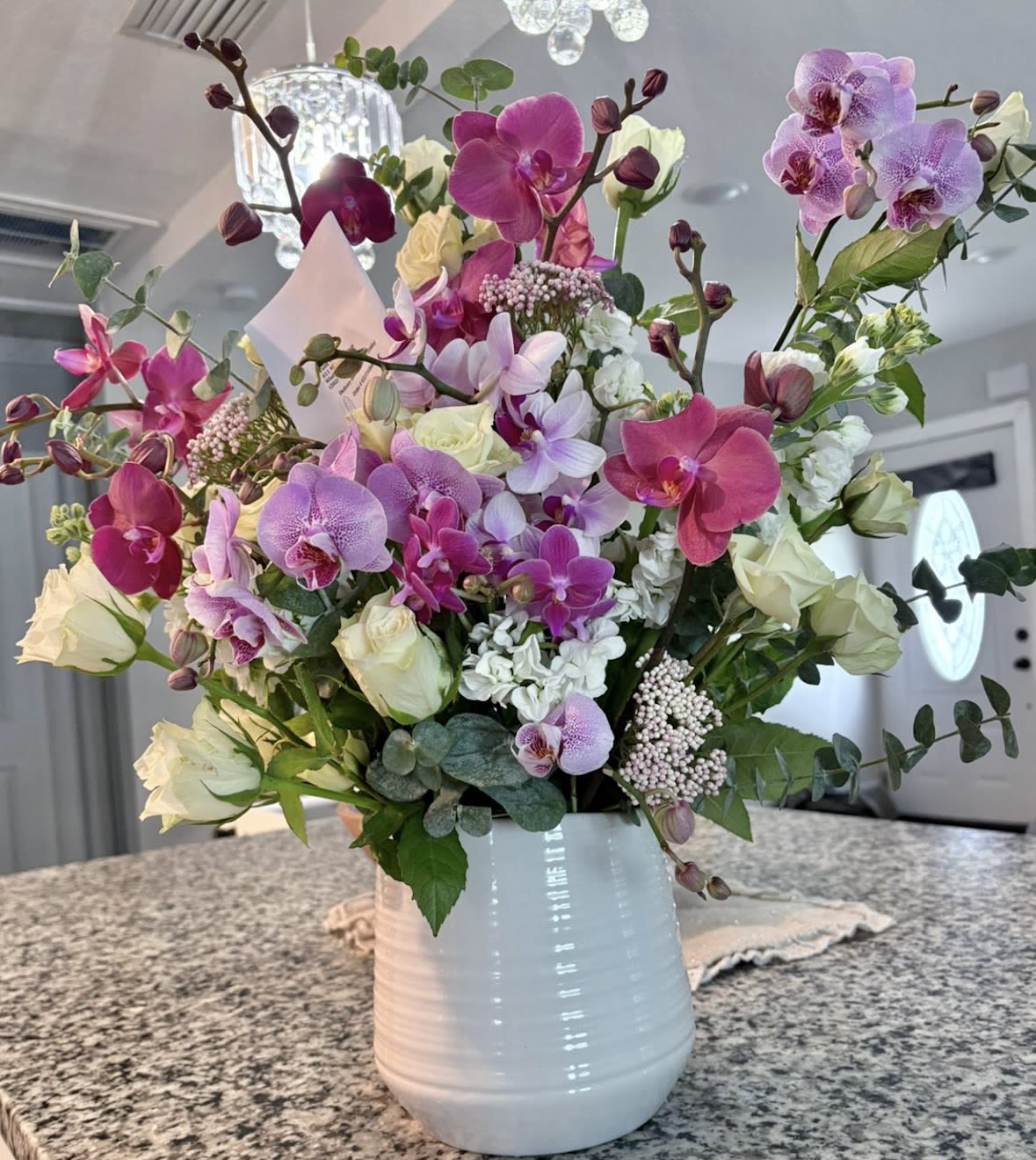 Tall arrangement of pink and purple orchids with white roses in a white ceramic vase