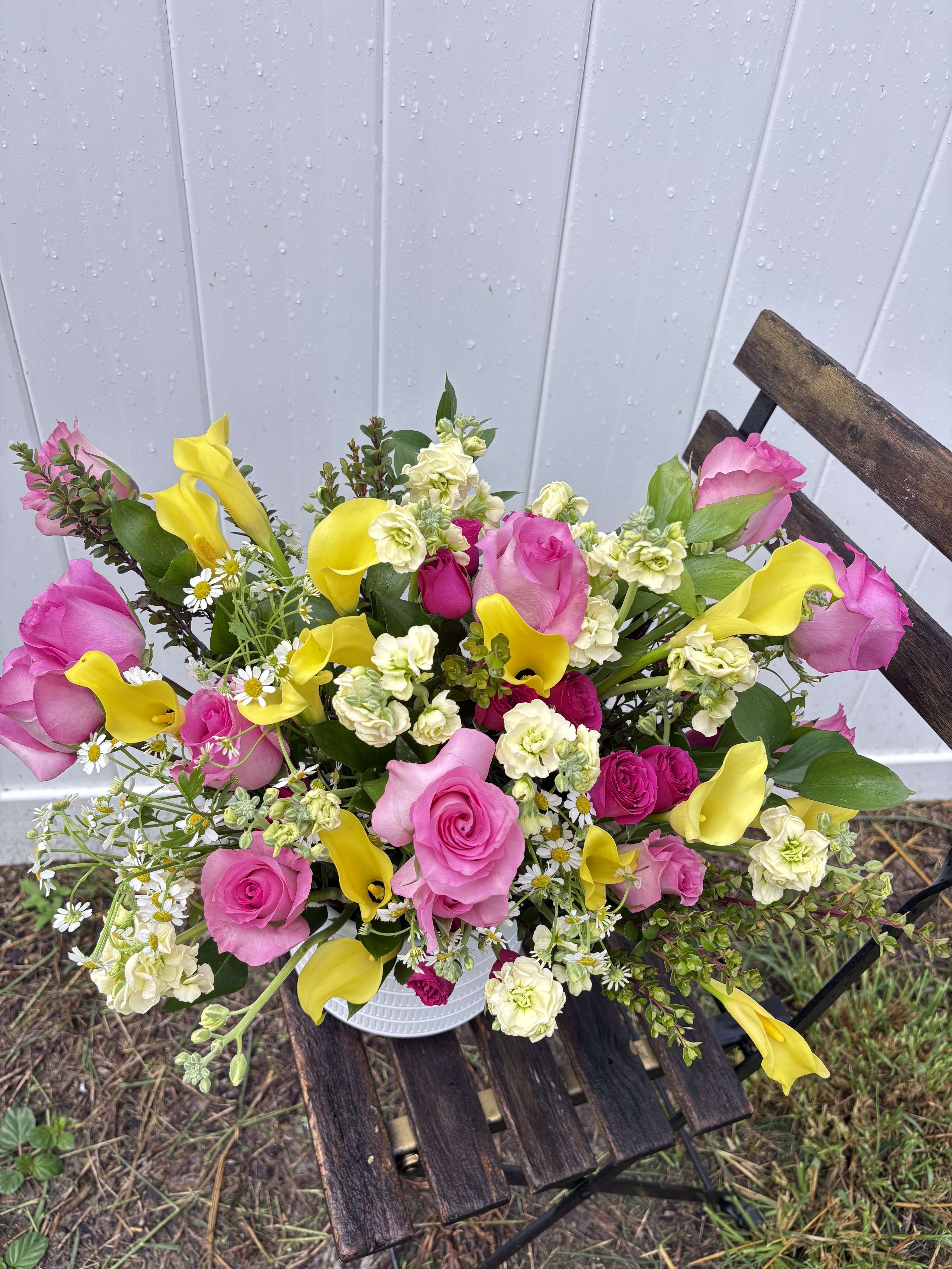 Bouquet of pink roses, yellow calla lilies, and small white flowers in a white container