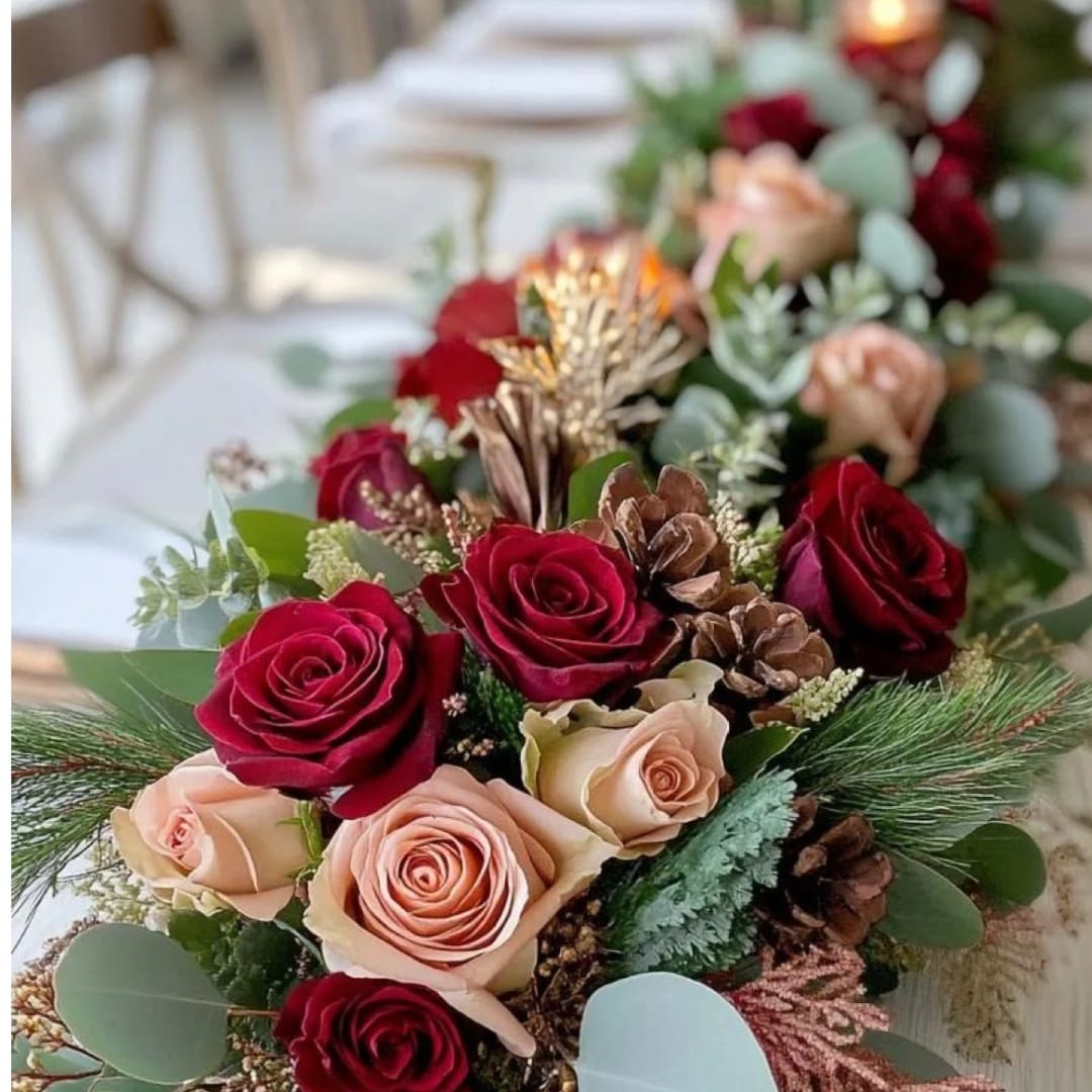 Red and blush roses arranged with pinecones and greenery on a table