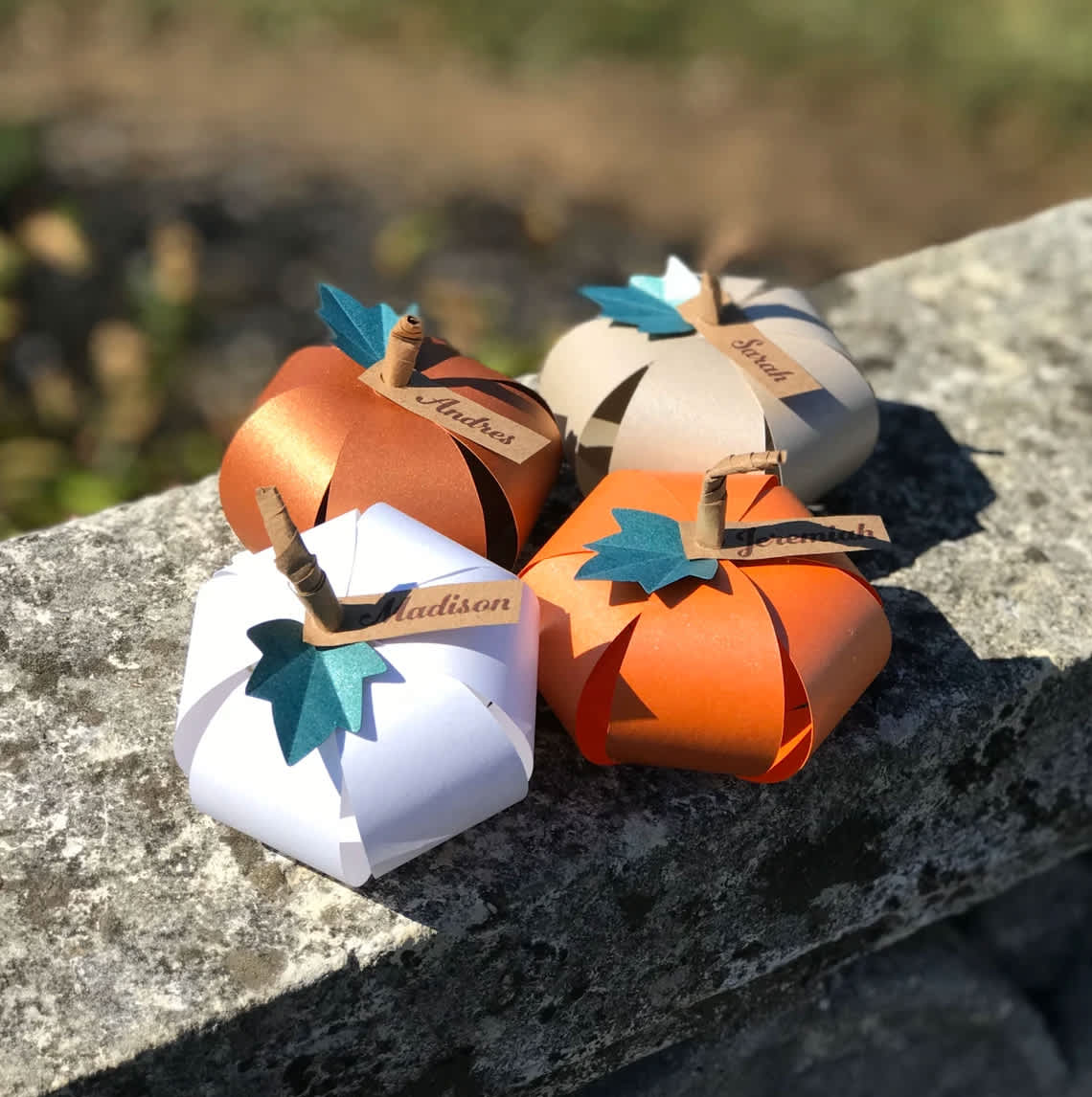 Four paper pumpkins with name tags arranged on a stone surface