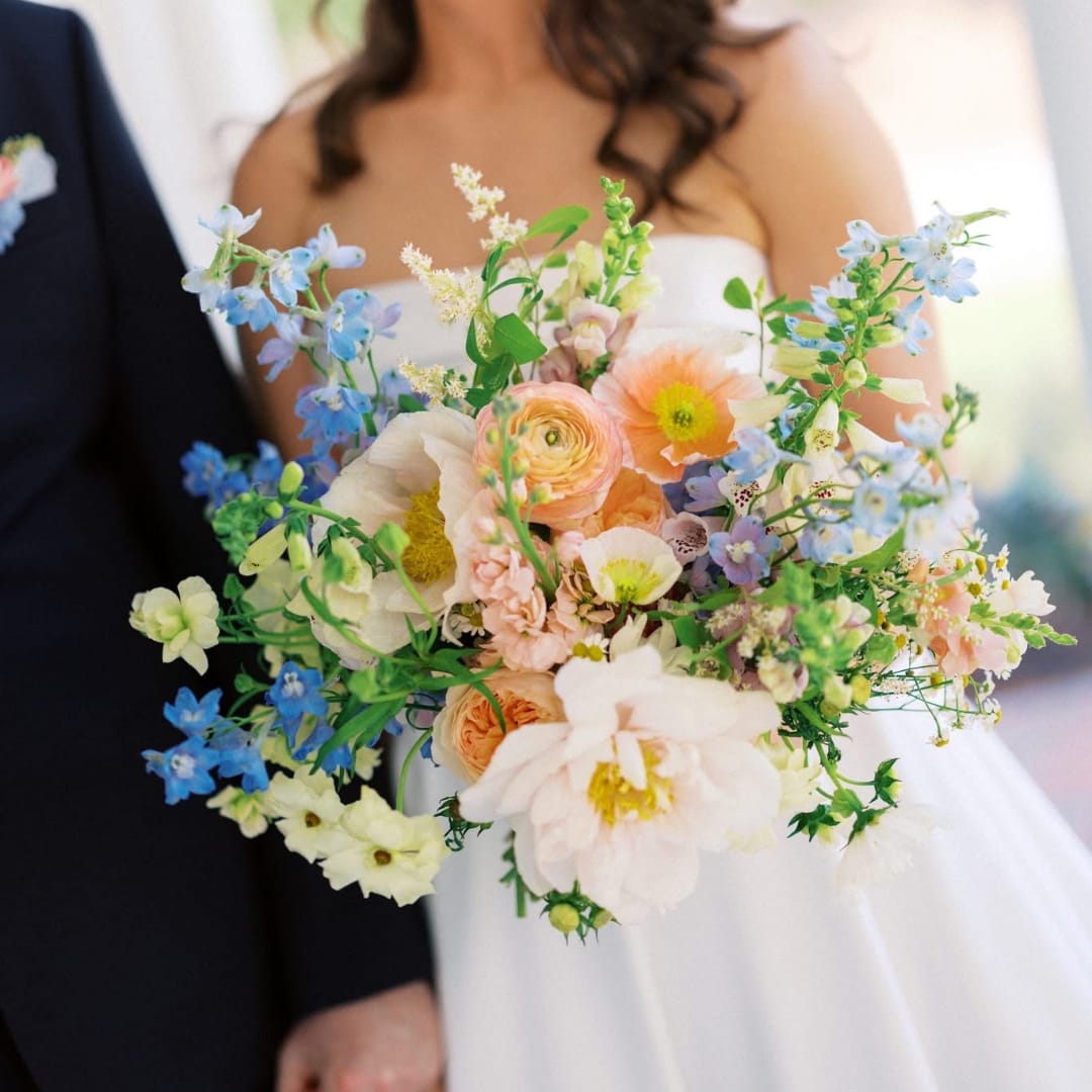 Bride holding a pastel bouquet with blue and peach flowers