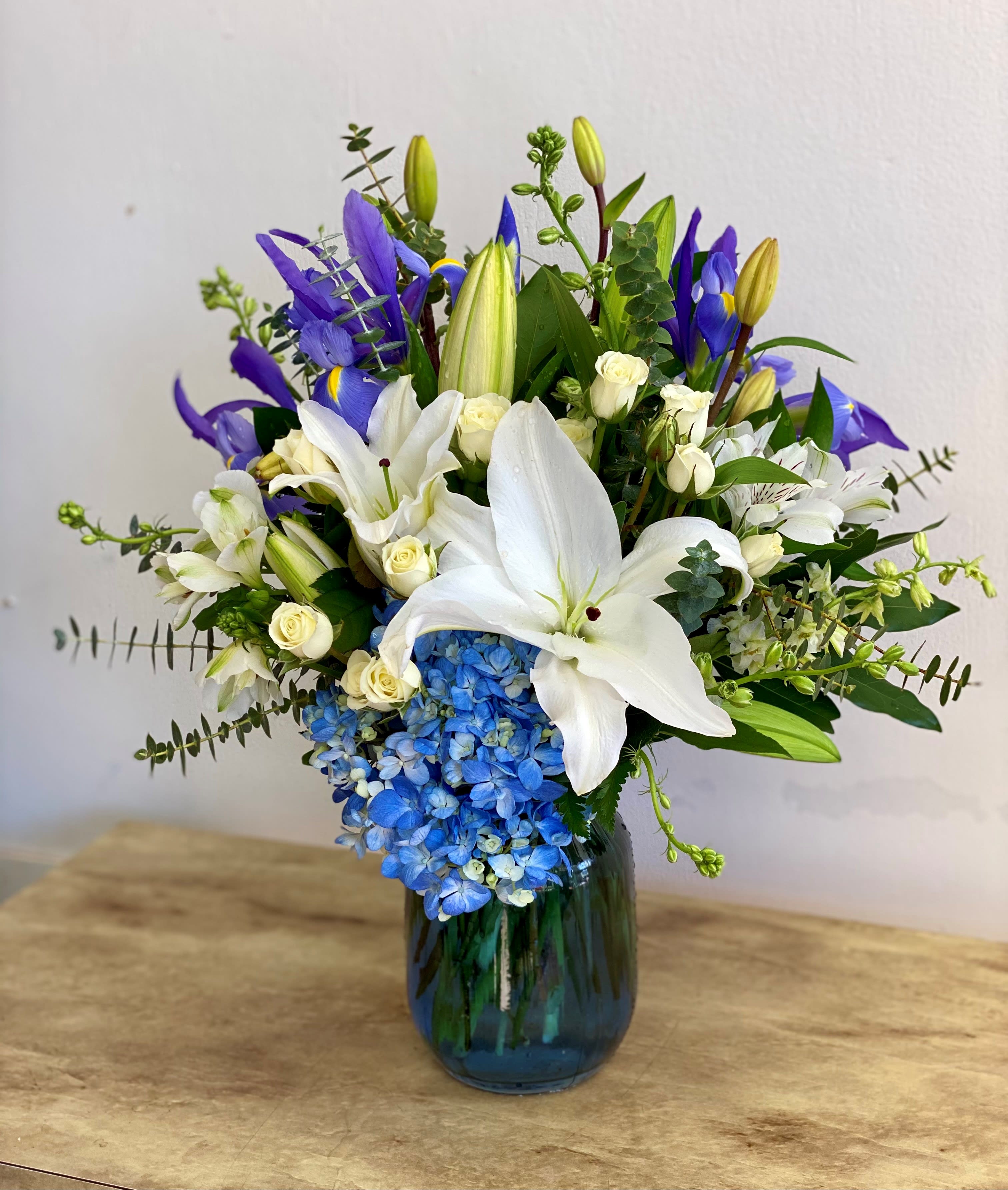 White lilies and blue hydrangeas in a glass vase with purple iris