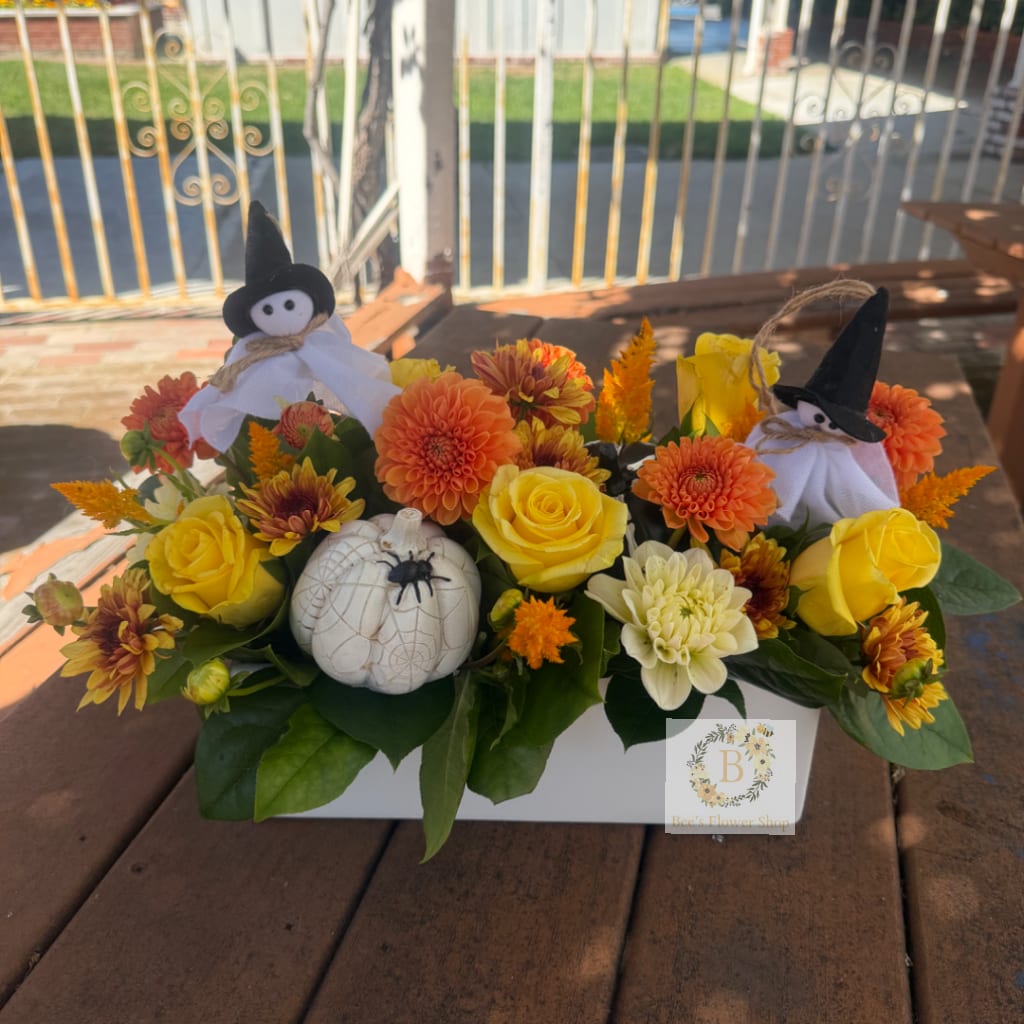 Halloween floral arrangement with yellow roses, orange blooms, and small witch decorations