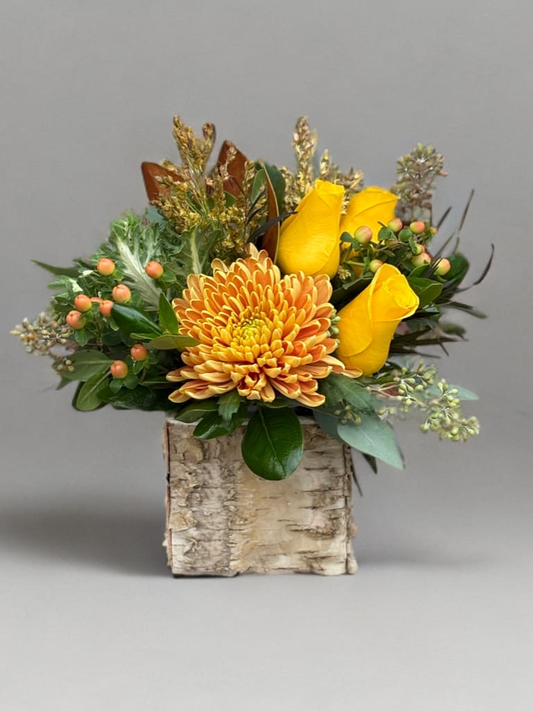 Yellow roses and an orange chrysanthemum in a birch container