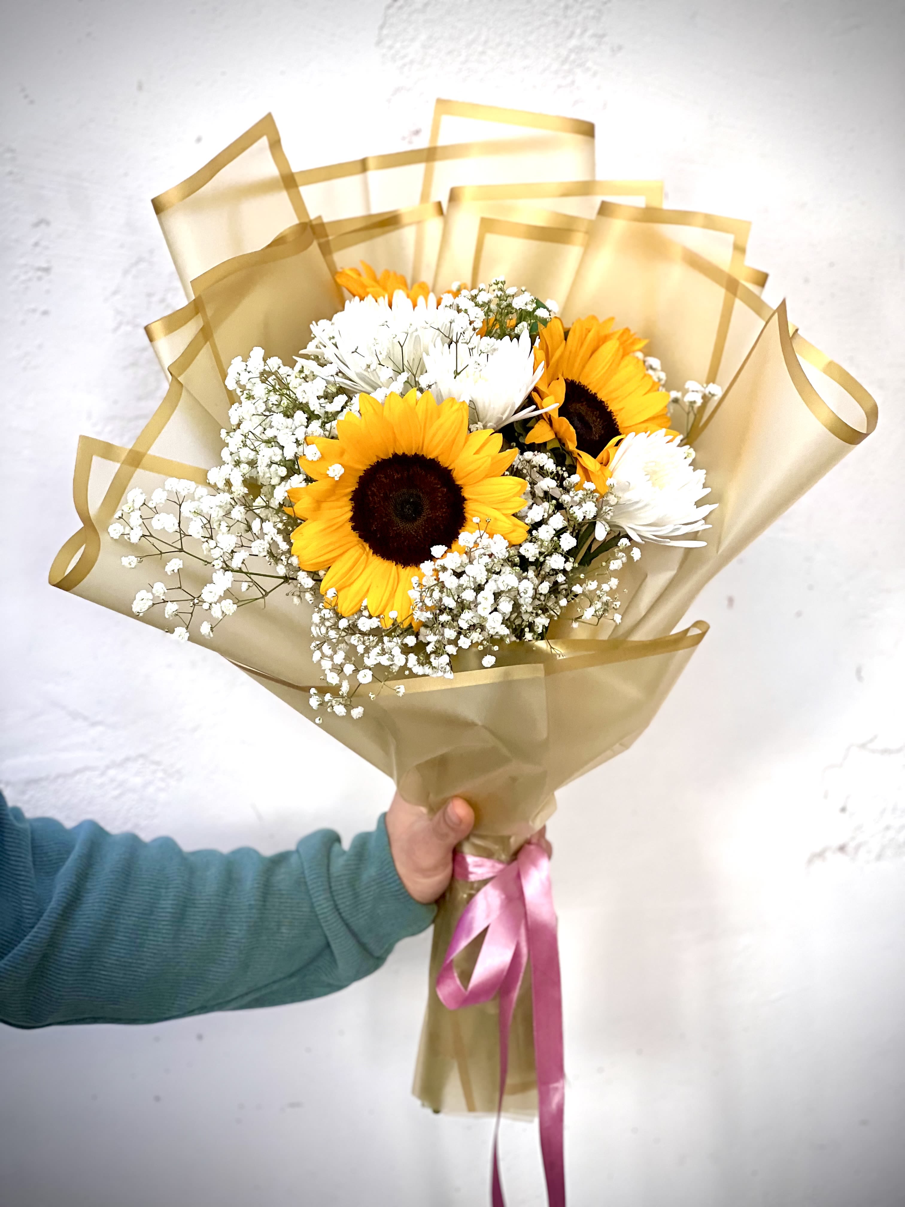 Bouquet of sunflowers and white daisies wrapped in gold paper with a pink ribbon