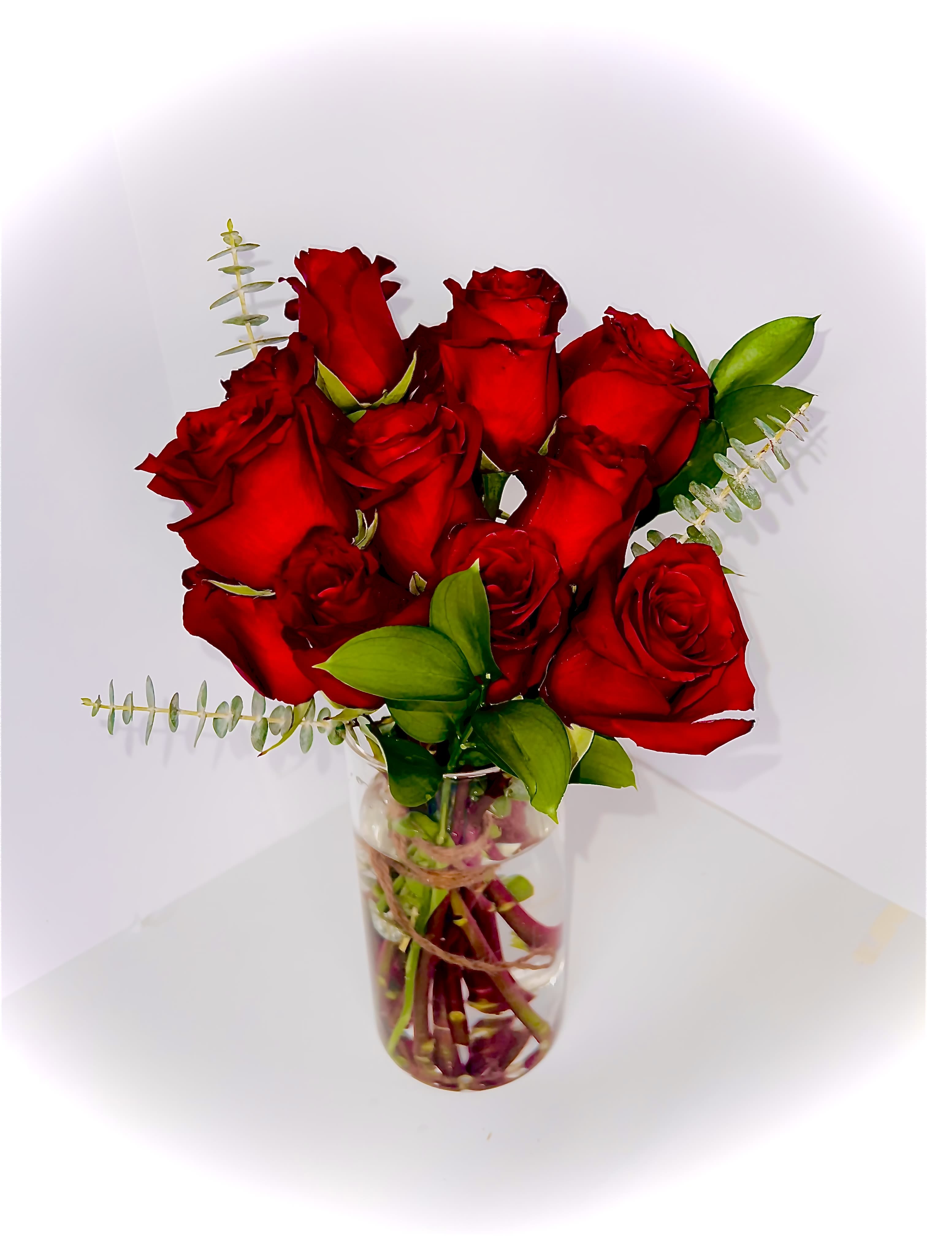 Red roses arranged in a clear glass vase with small greenery accents