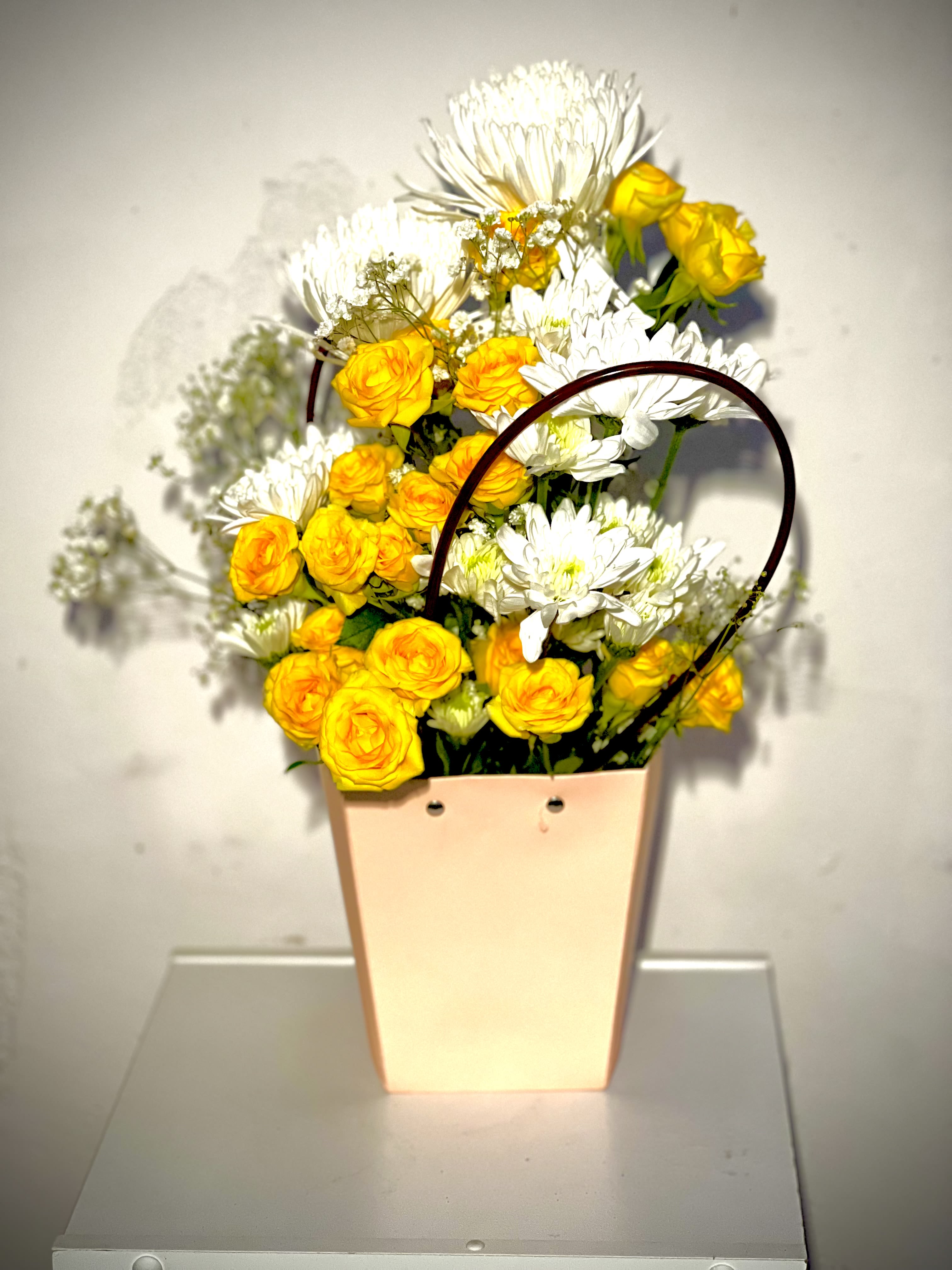 Yellow roses and white daisies in a peach tote-style container