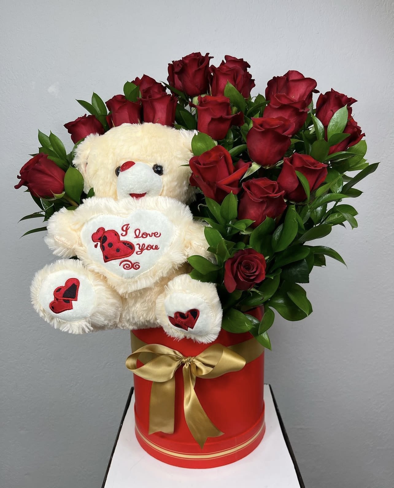 Red roses arranged with a teddy bear in a red gift box