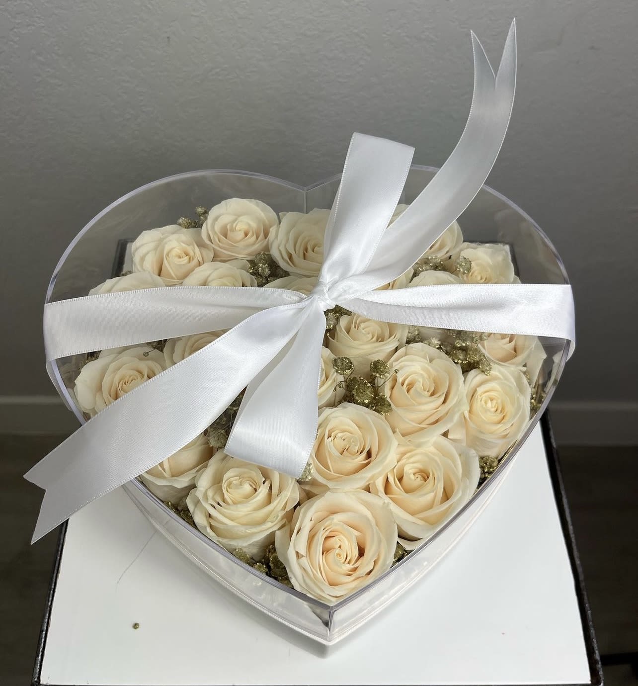 Cream roses in a clear heart-shaped box tied with a white ribbon