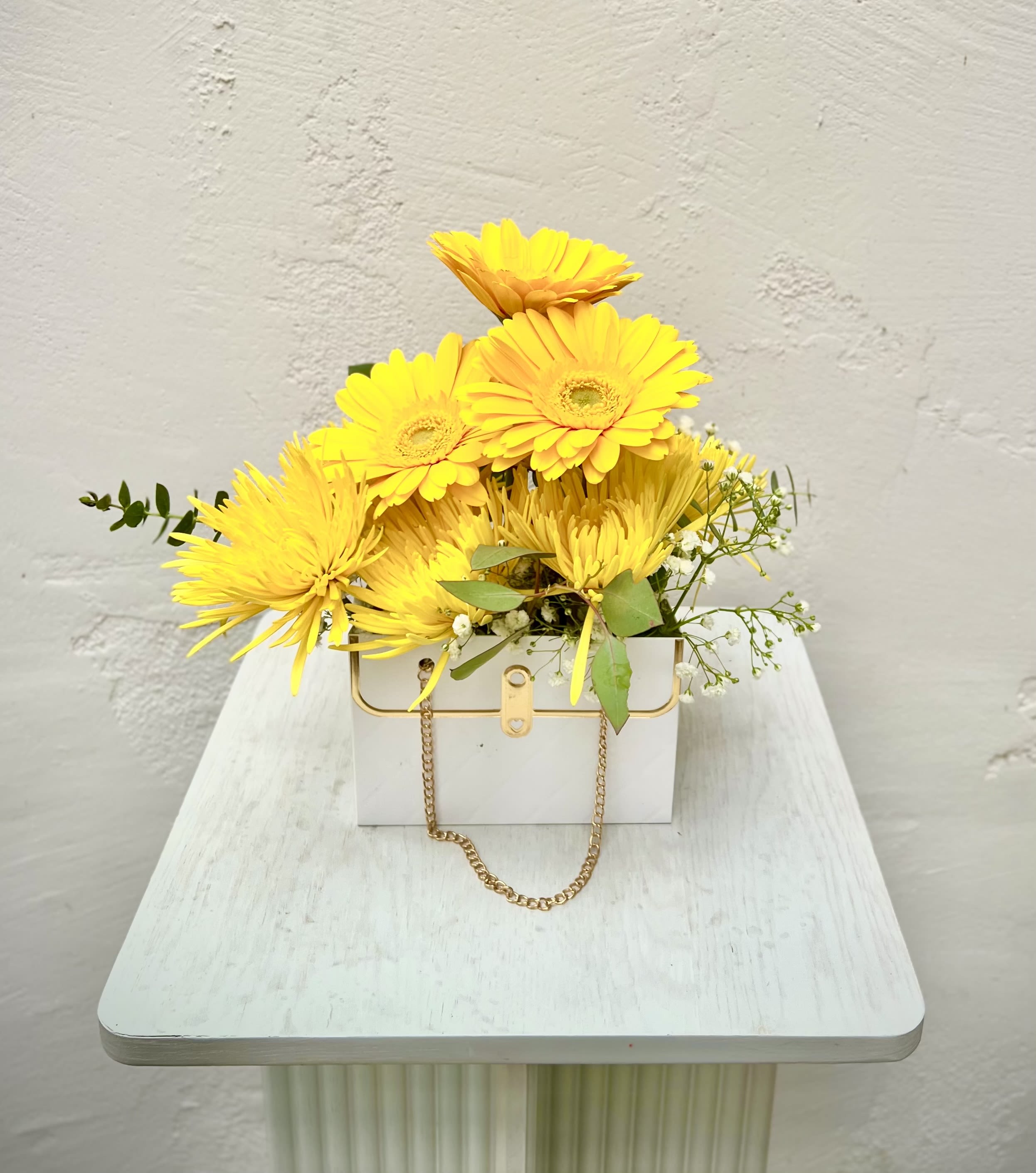 Yellow gerbera daisies in a white box with a gold chain handle