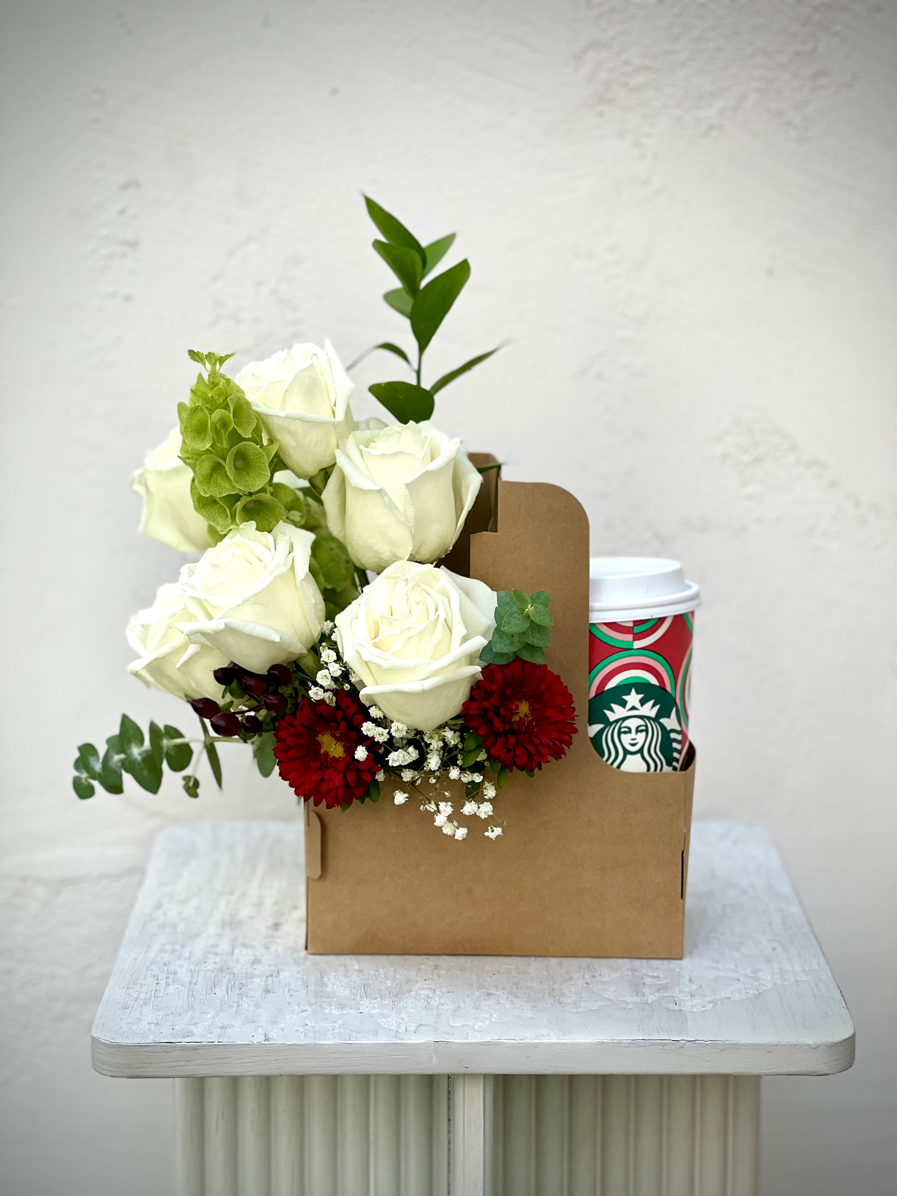 White roses with red flowers in a brown gift box beside a Starbucks cup