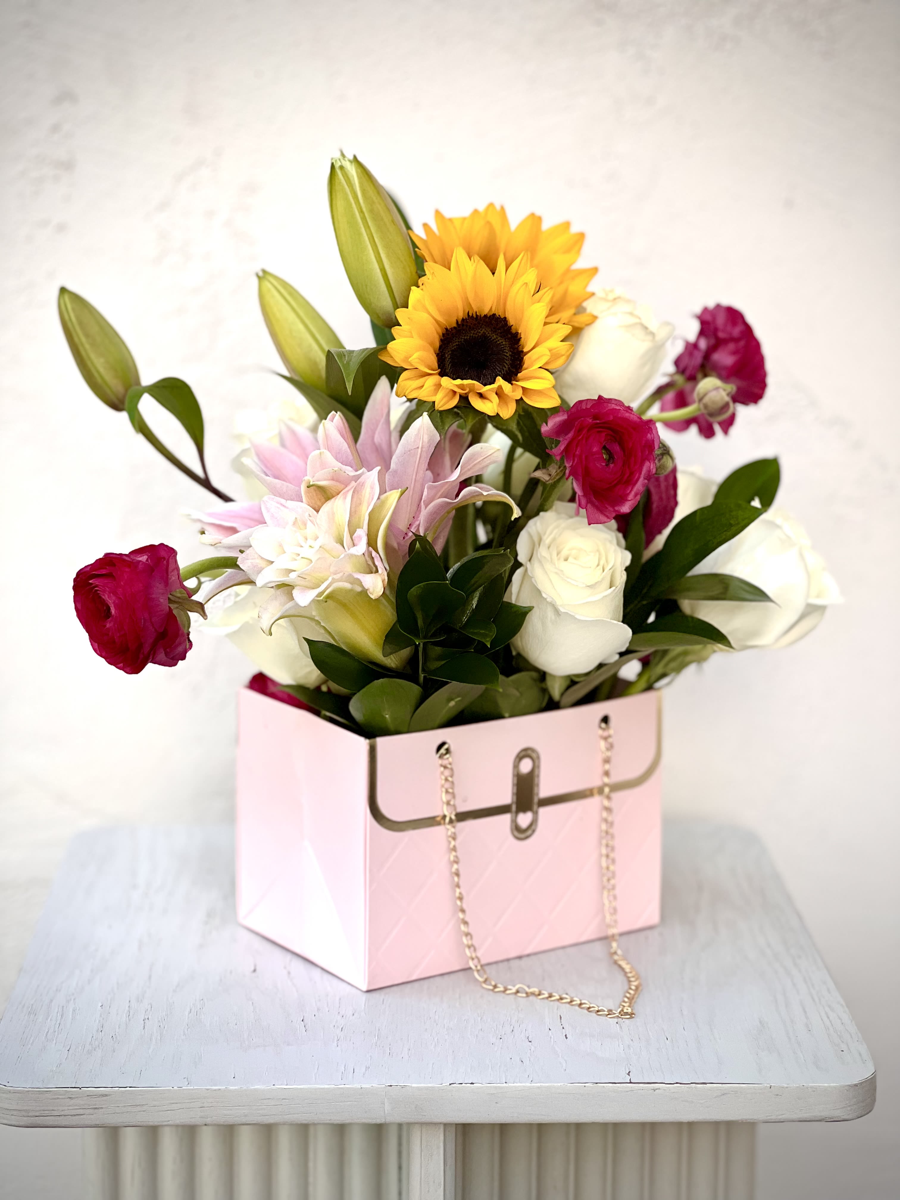 Mixed bouquet in a pink gift box with sunflowers, roses, lilies, and ranunculus