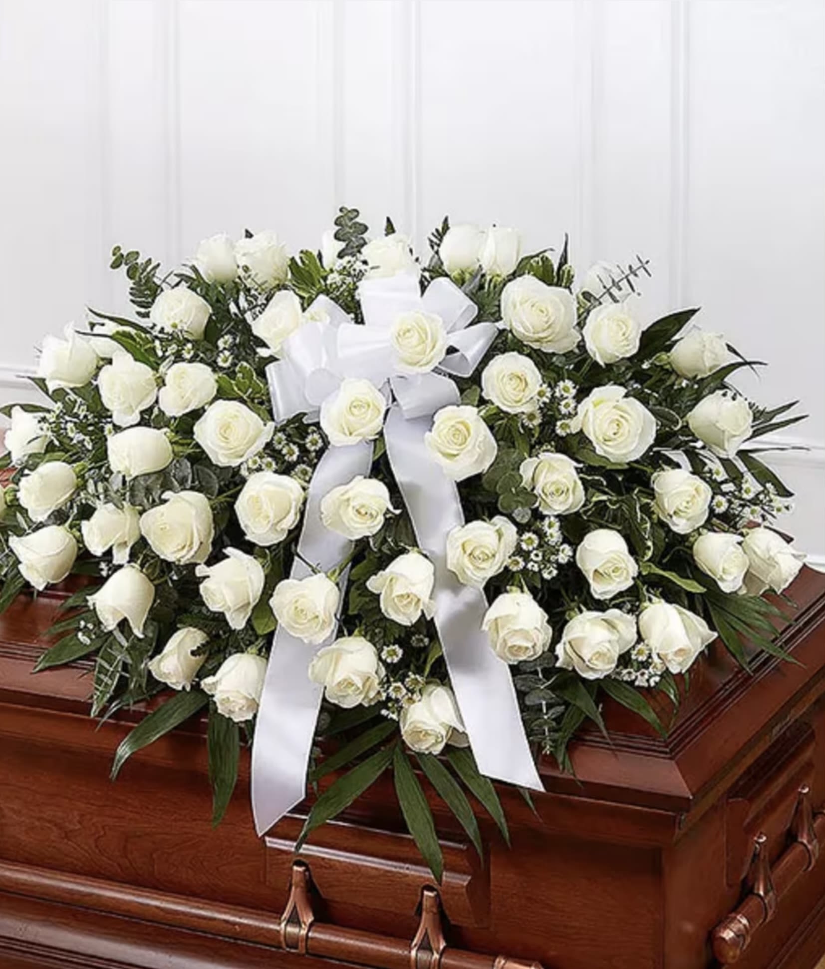 White rose casket spray with a white ribbon on a wooden casket