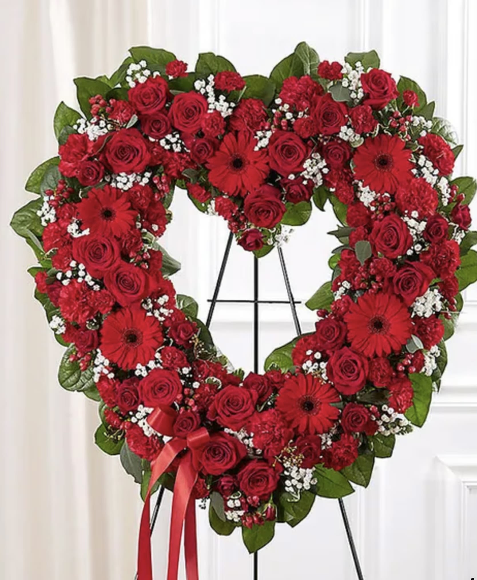 Heart-shaped red rose wreath on a stand with a ribbon bow