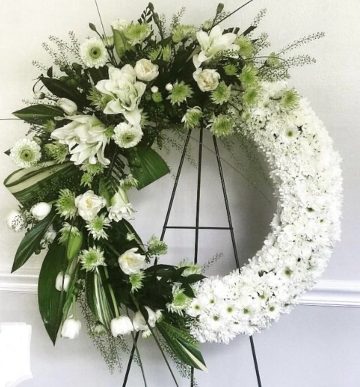 White floral wreath on a black stand with mixed blooms and greenery