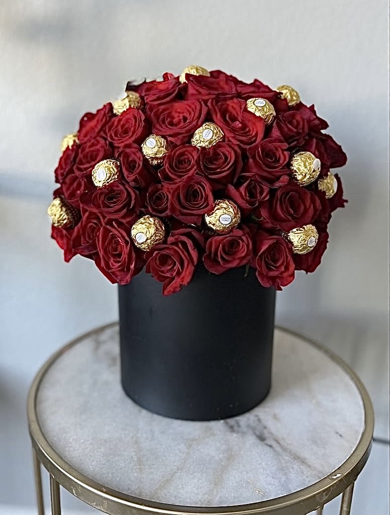 Red roses arranged with gold-wrapped chocolates in a black box