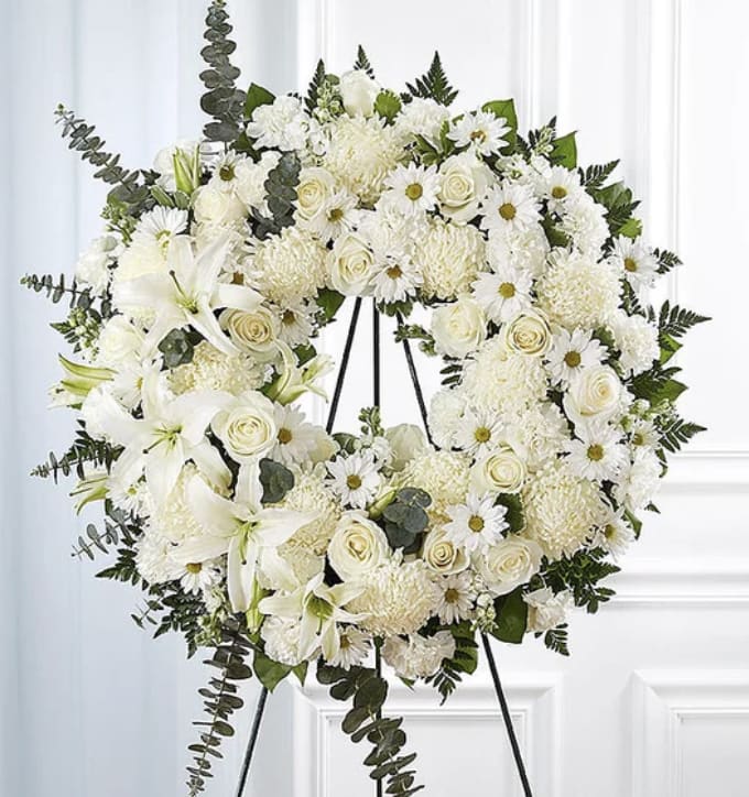 White funeral wreath on a black stand with roses, daisies, and lilies