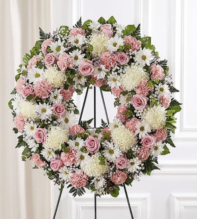 Pink and white floral wreath on a black stand