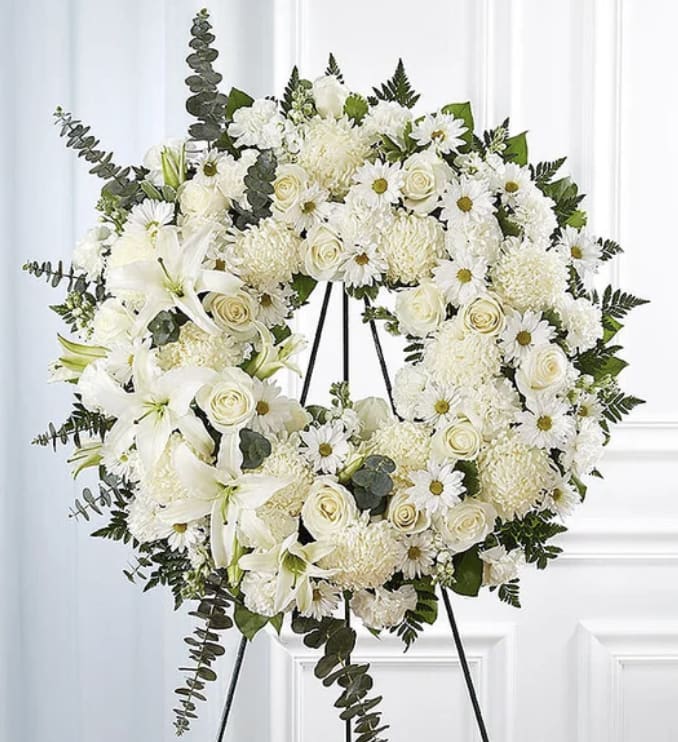 White floral wreath on a black stand with roses, daisies, and lilies