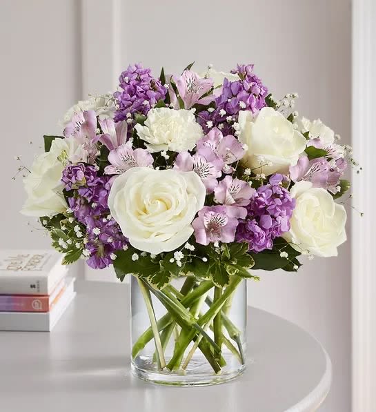 White roses and purple flowers arranged in a clear glass vase