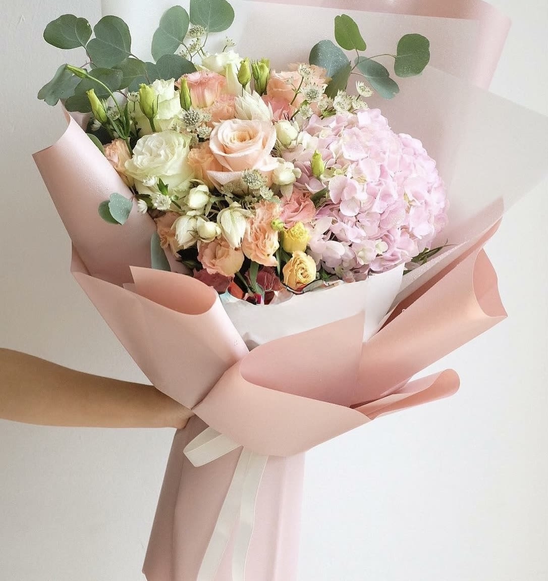 Hand-tied bouquet of pink and cream flowers wrapped in blush paper