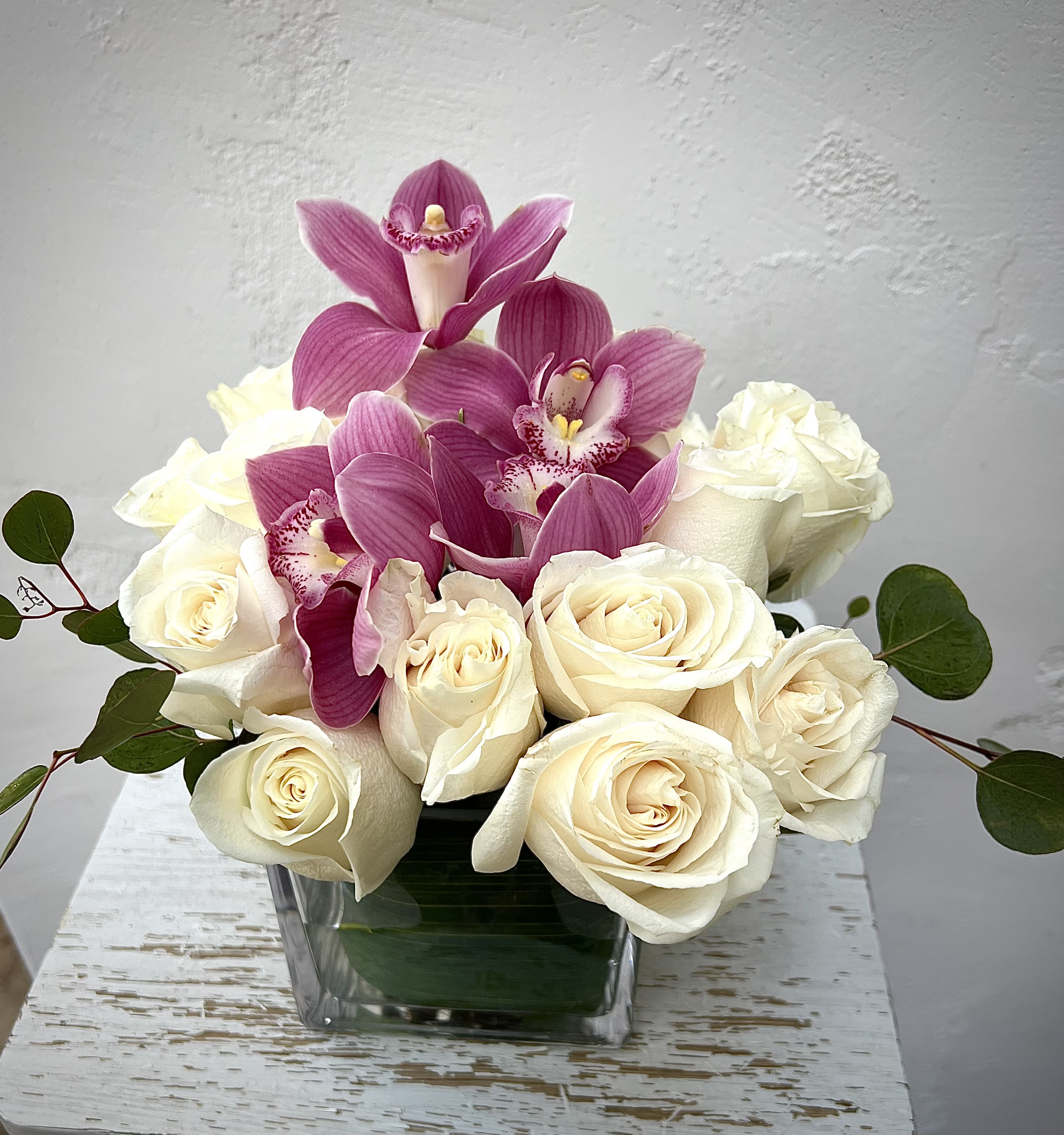 White roses with pink orchids in a square glass vase