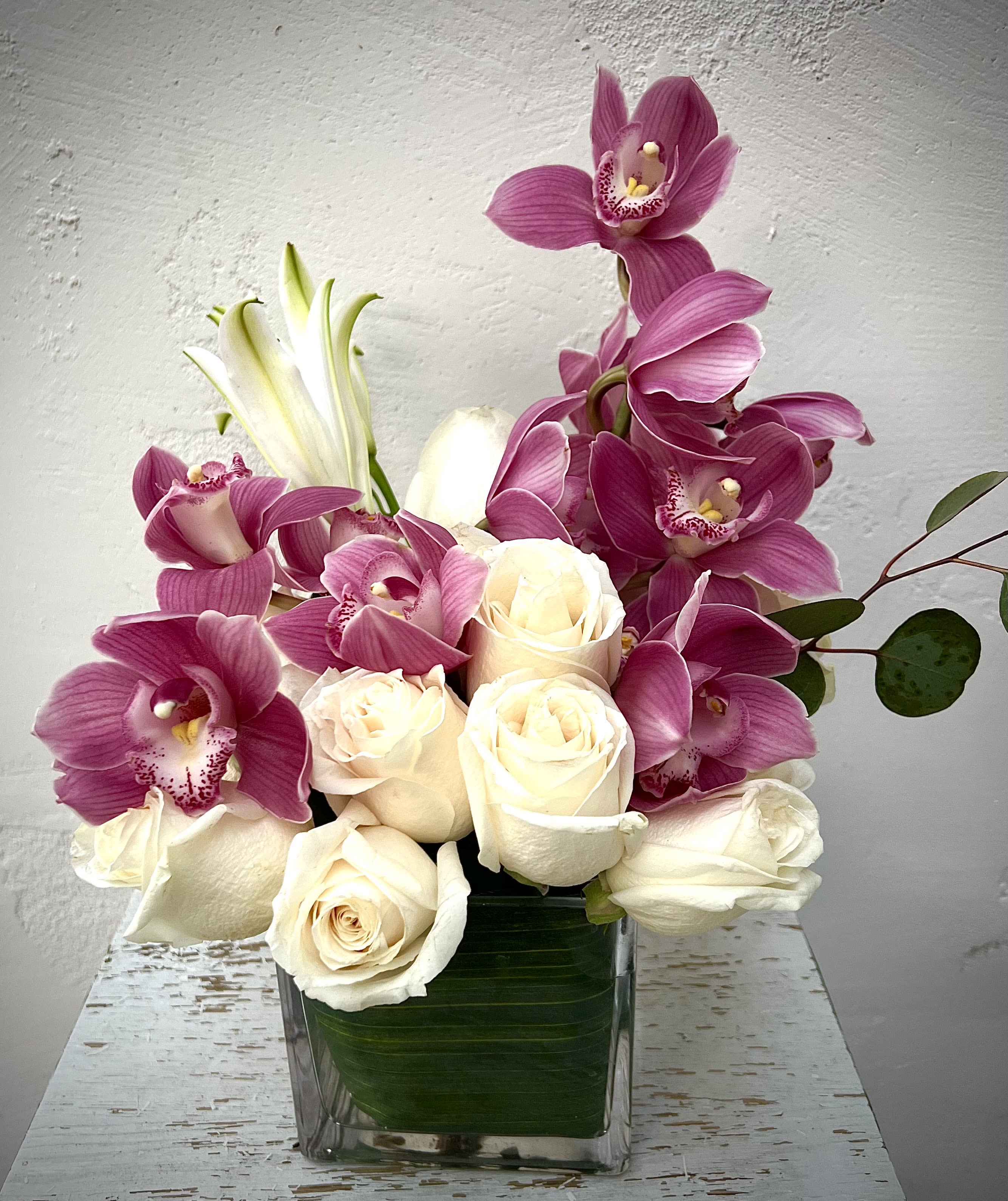 Pink orchids and white roses arranged in a clear square vase