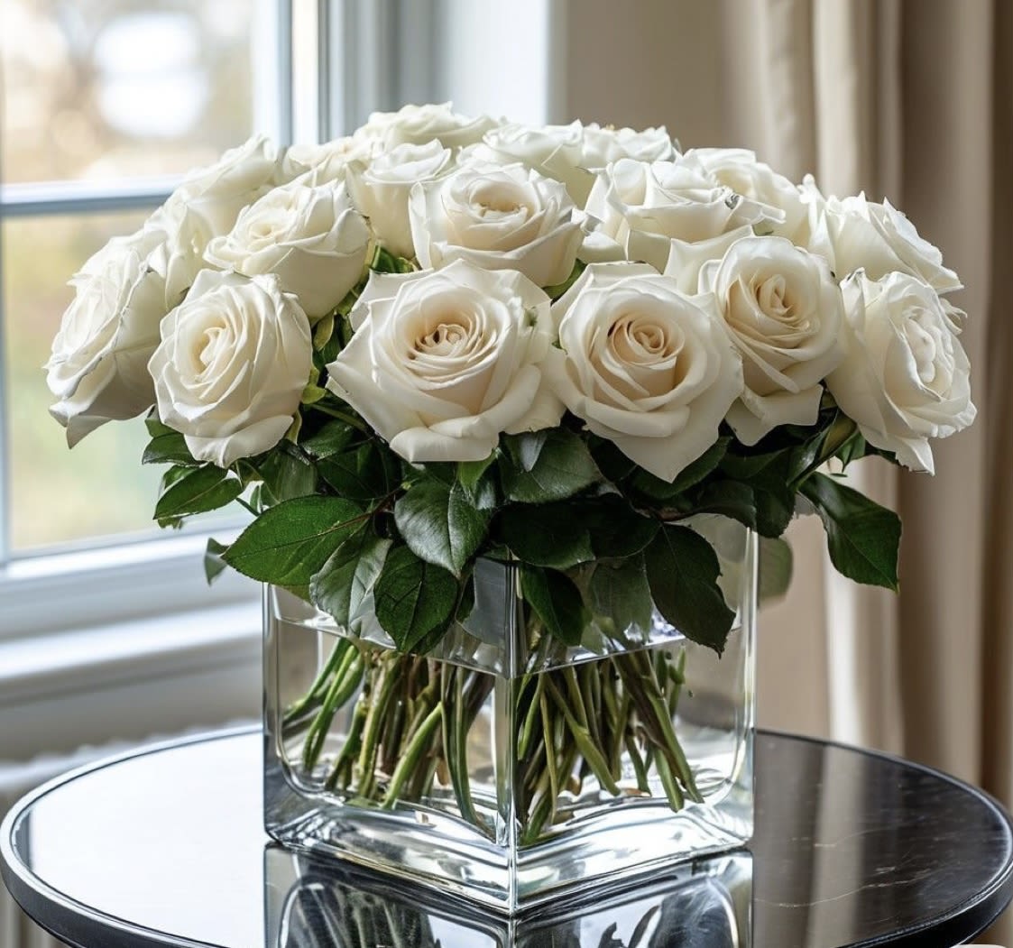 White roses arranged in a clear square glass vase