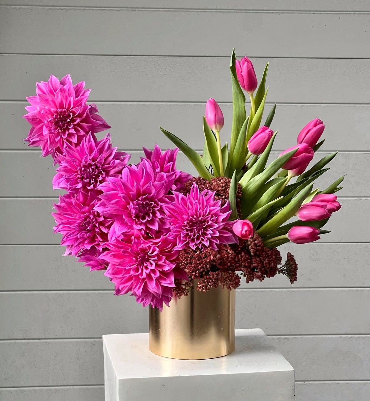 Pink dahlias and tulips arranged in a gold vase