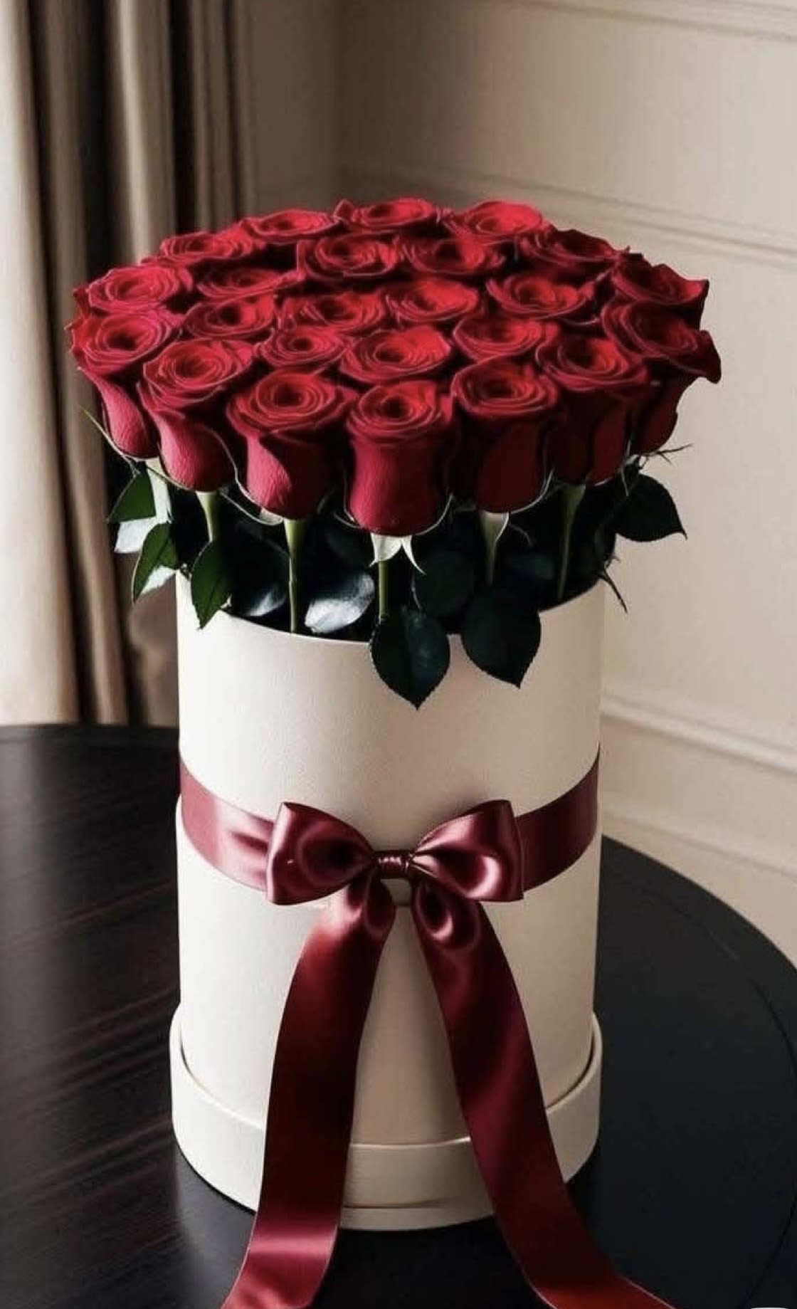 Red roses arranged in a white hat box with a burgundy ribbon