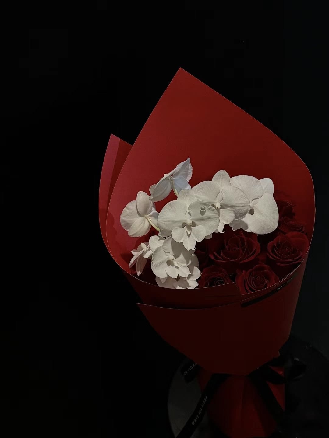 Bouquet of red roses and white orchids wrapped in red paper