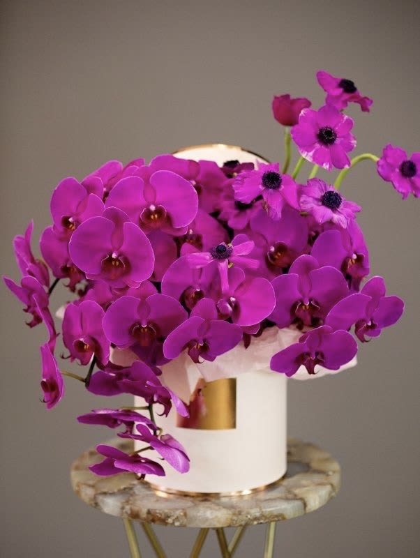 Bright magenta orchids arranged in a white hatbox vase