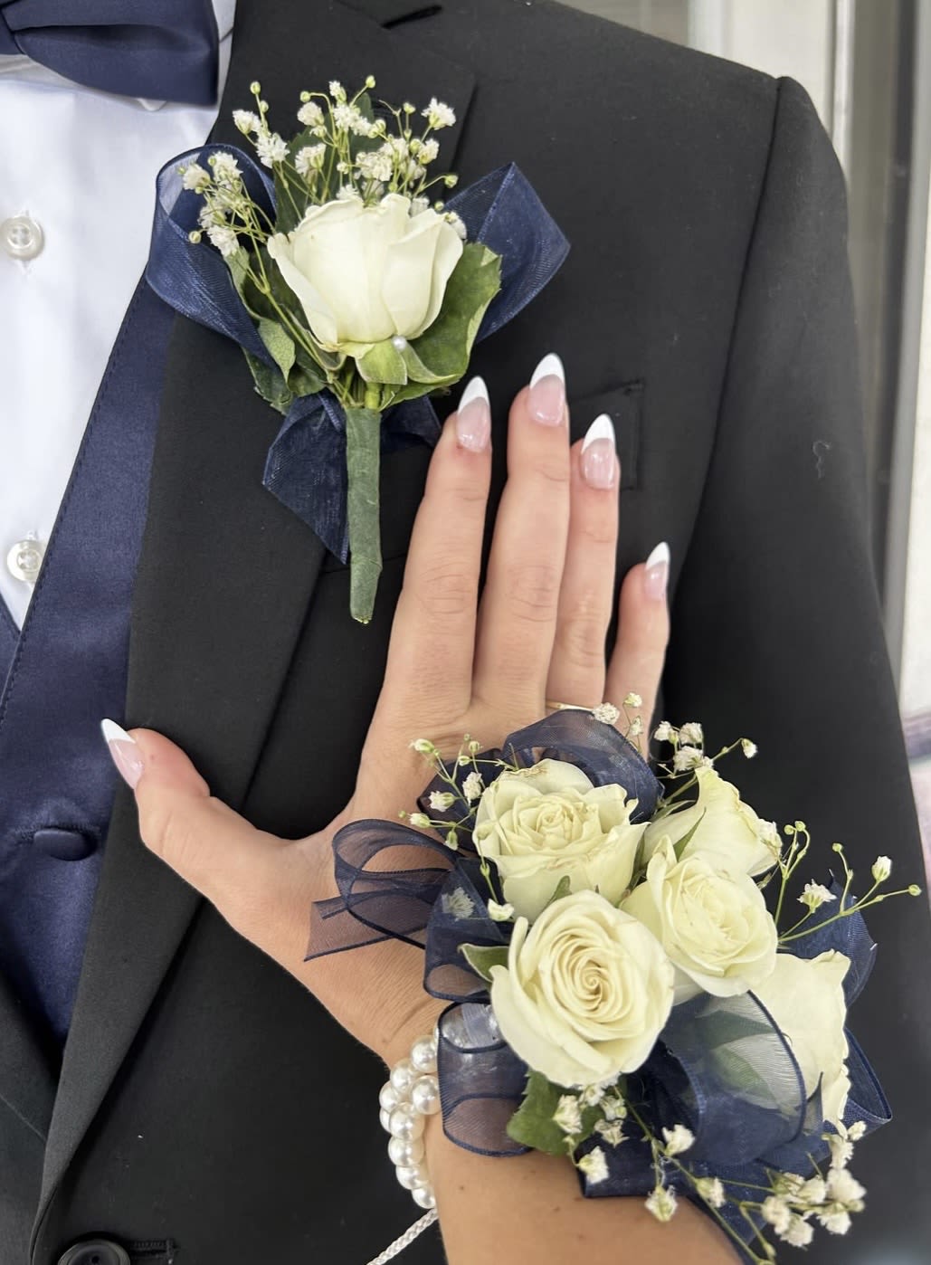 Midnight Ivory Romance Same Day Delivery  - Midnight Ivory Romance Elegant, timeless, and beautifully coordinated — our “Midnight Ivory Romance” corsage and boutonniere set is designed to make every special occasion unforgettable. Featuring fresh ivory roses, delicate baby’s breath, and luxurious navy ribbon accents, this floral pair adds a refined and romantic touch to proms, weddings, engagements, and formal celebrations.  A perfect combination of classic beauty and modern sophistication for couples who want to shine together in style.
