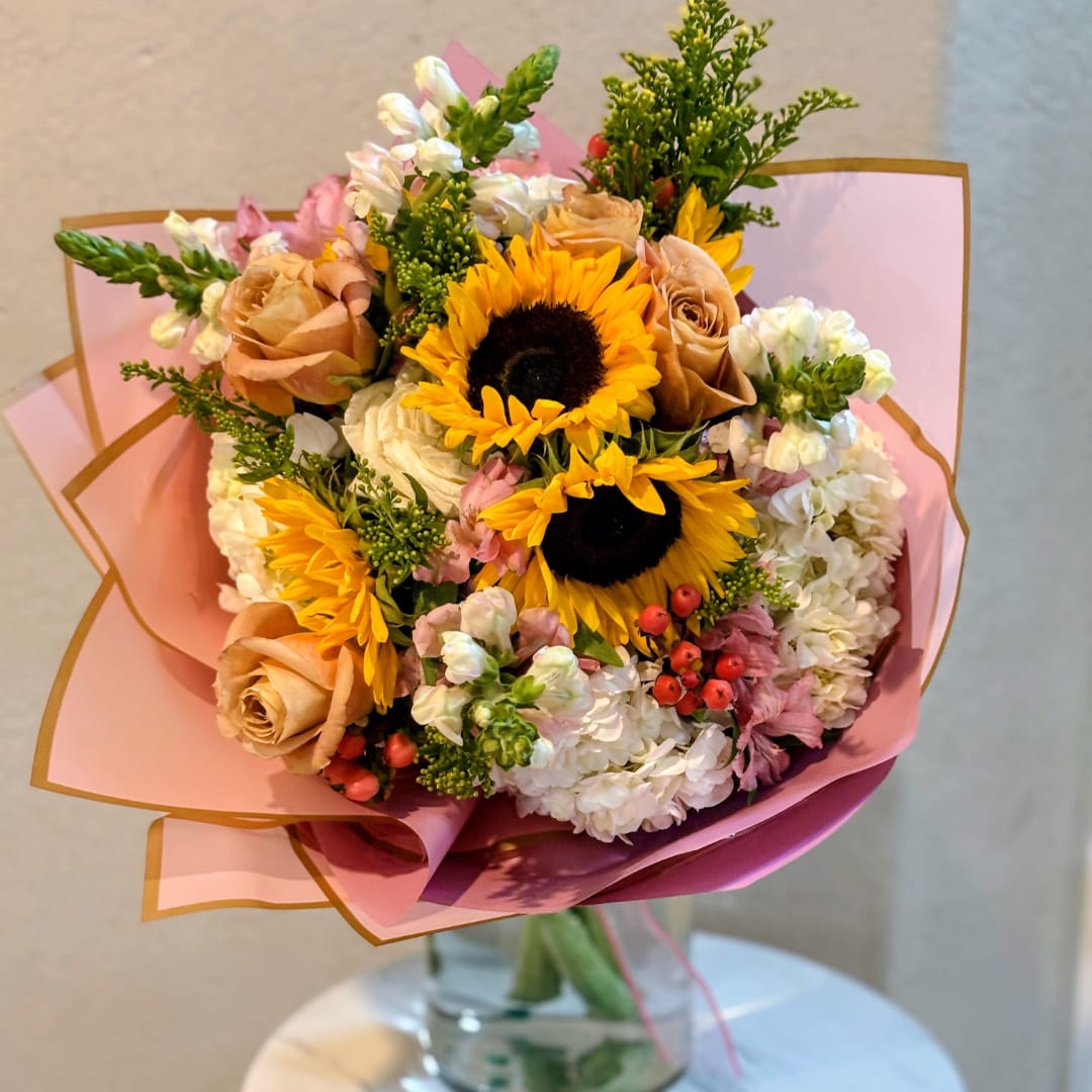 Bouquet of sunflowers, roses, and white blooms wrapped in pink paper