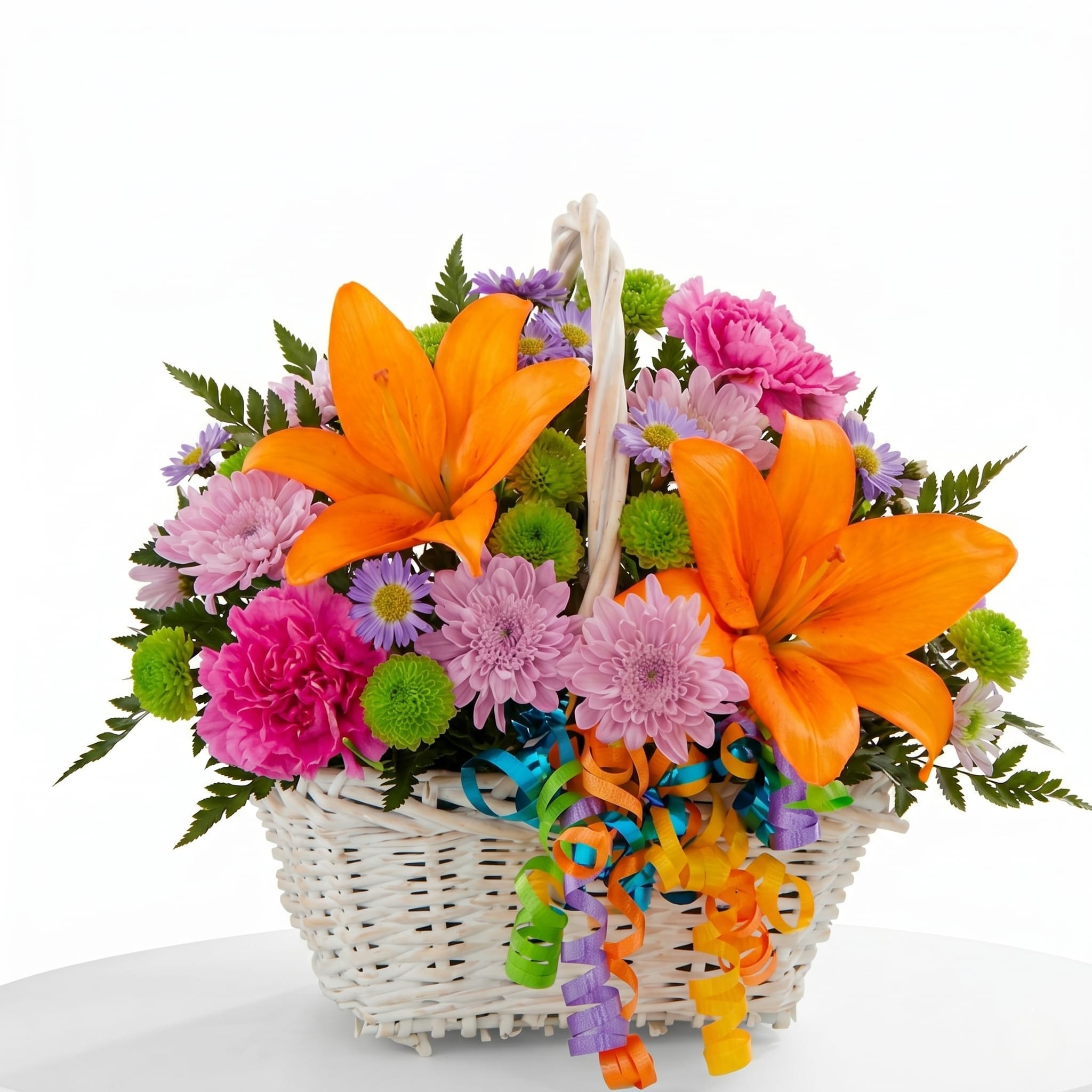 Fiesta Basket Bouquet - Bring the celebratory spirit of the River Walk straight to someone's door! This eye-catching woven basket is bursting with a lively mix of bold orange lilies, hot pink carnations, and lavender daisy pompons. Finished with a playful cascade of colorful curling ribbons, it’s a vibrant, ready-to-display arrangement perfect for birthdays, thank-yous, or just because.