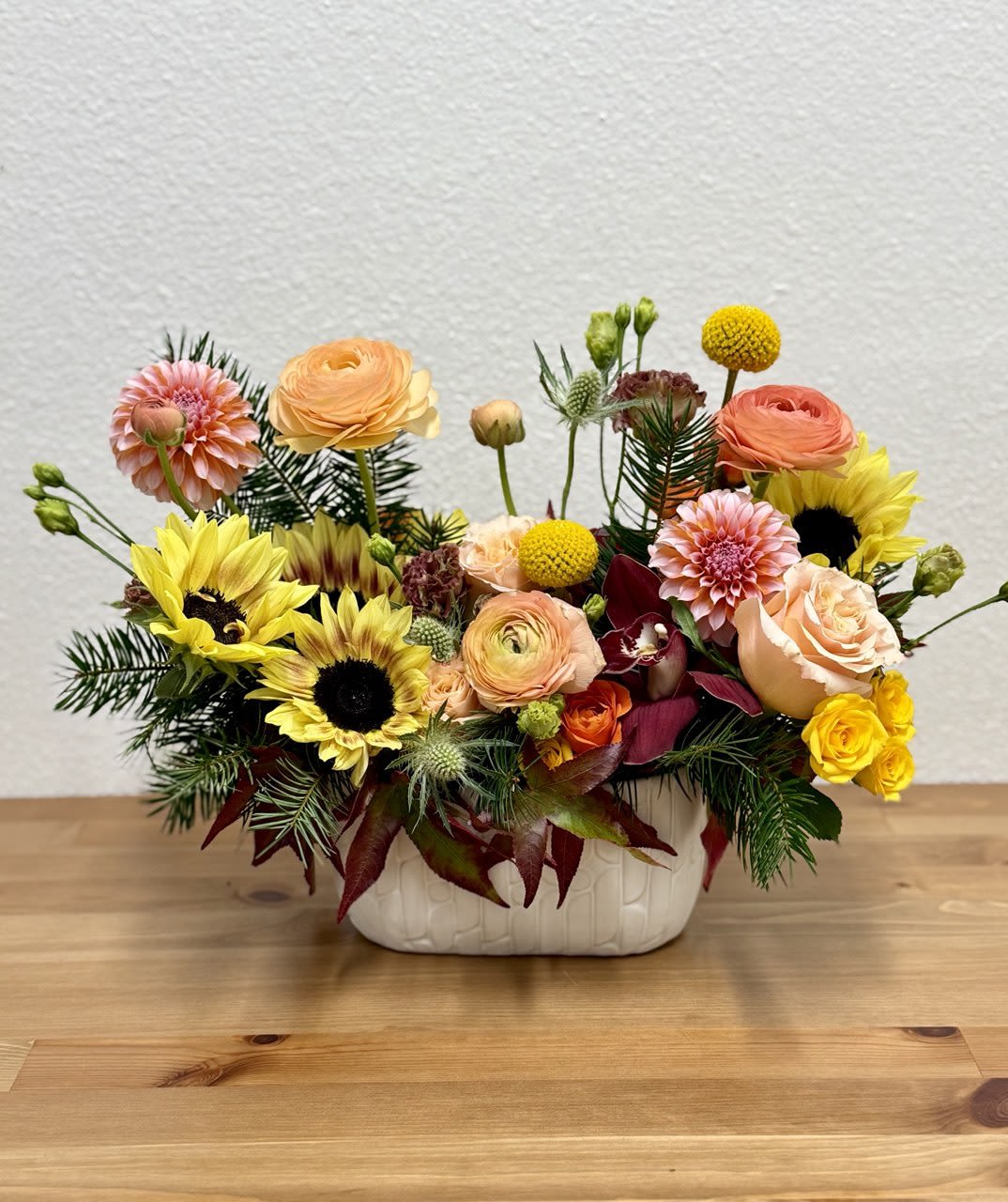 Mixed bouquet of sunflowers, roses, and dahlias in a white ceramic vase
