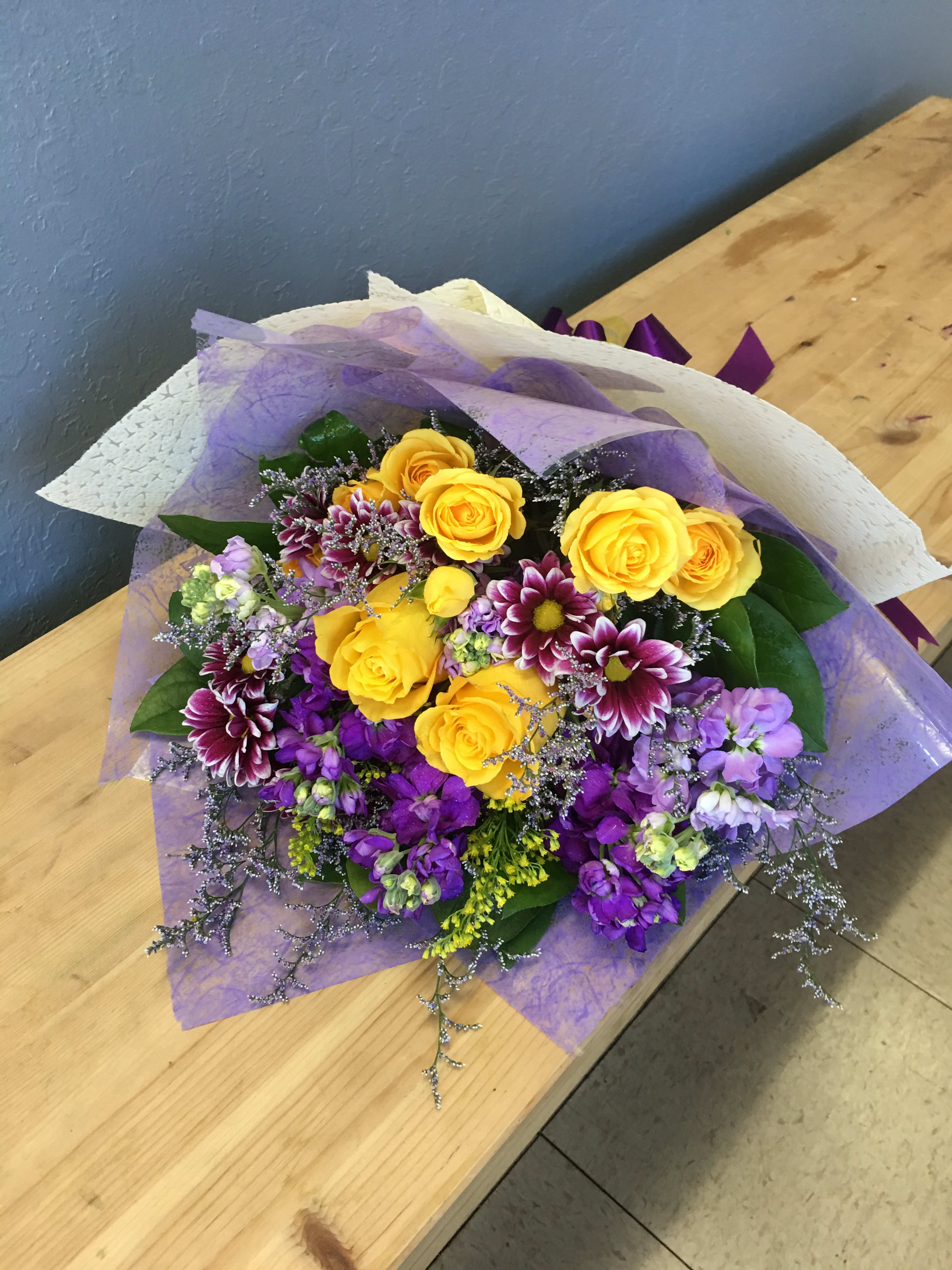 Bouquet of yellow roses and purple flowers wrapped in lavender paper