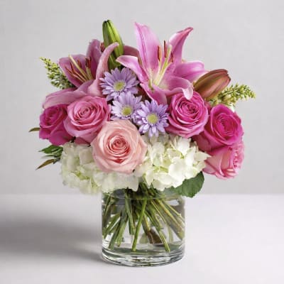 Pink lilies, roses, and lavender daisies in a clear glass vase