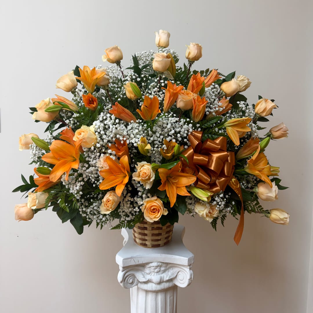 Orange lilies and peach roses in a woven basket on a pedestal